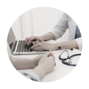 Doctor or healthcare professional typing on a laptop at a desk while consulting with a patient.