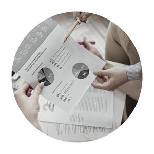 Two people reviewing financial or business reports with pie charts and data on paper documents.