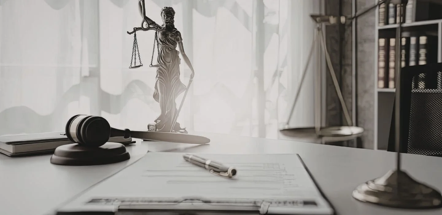 A desk with a judge's gavel, a law book, a pen, and a scale of justice in the background.