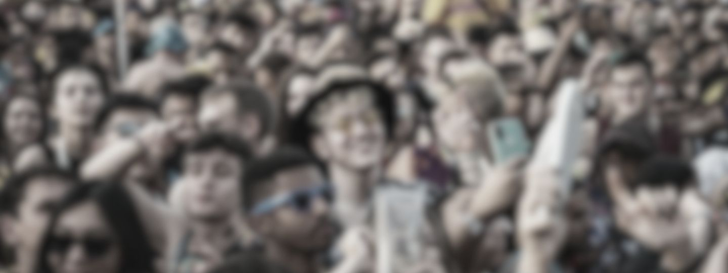 A large crowd of people taking photos with their smartphones, many wearing glasses and hats.