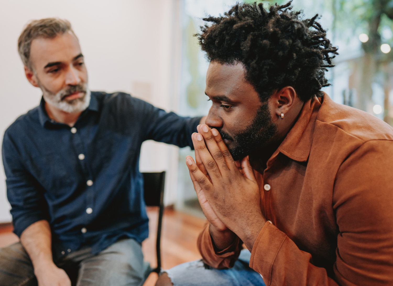 A mentor rests a supportive hand on the shoulder of a man deep in thought