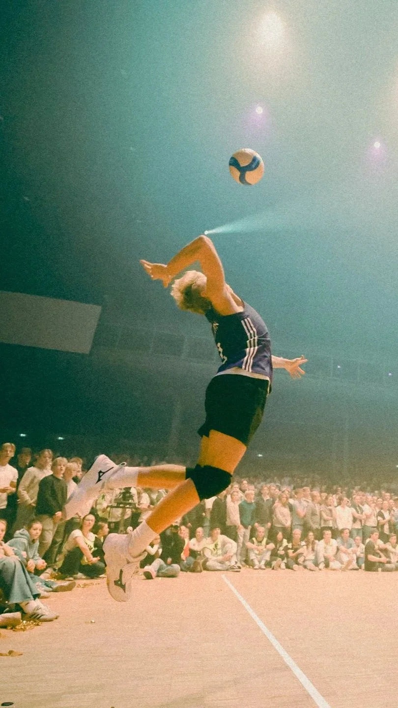 En volleyballspiller hopper høyt for å slå ballen under en kamp foran et publikum.