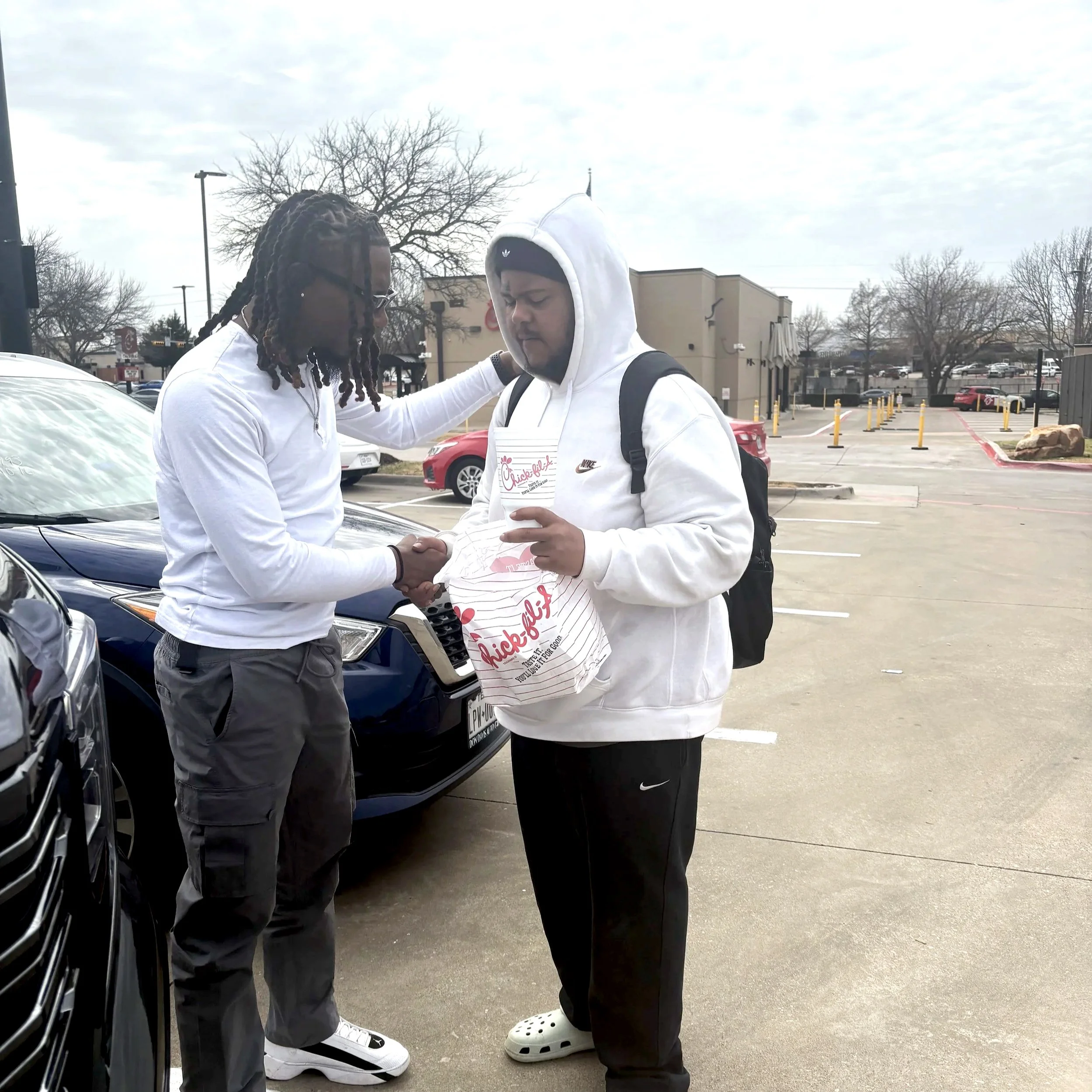 Two men standing in a parking lot praying.