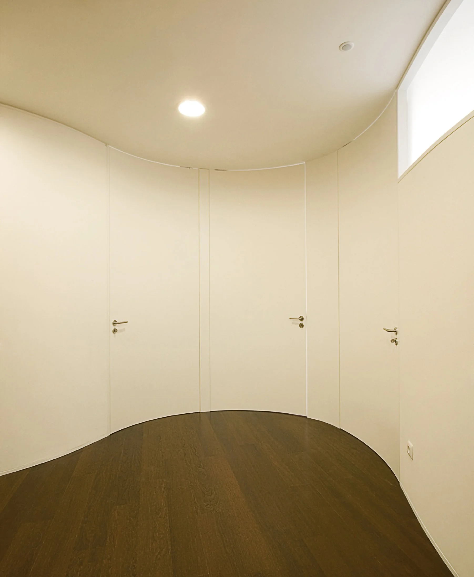Corredor com portas brancas curvas e piso de madeira
