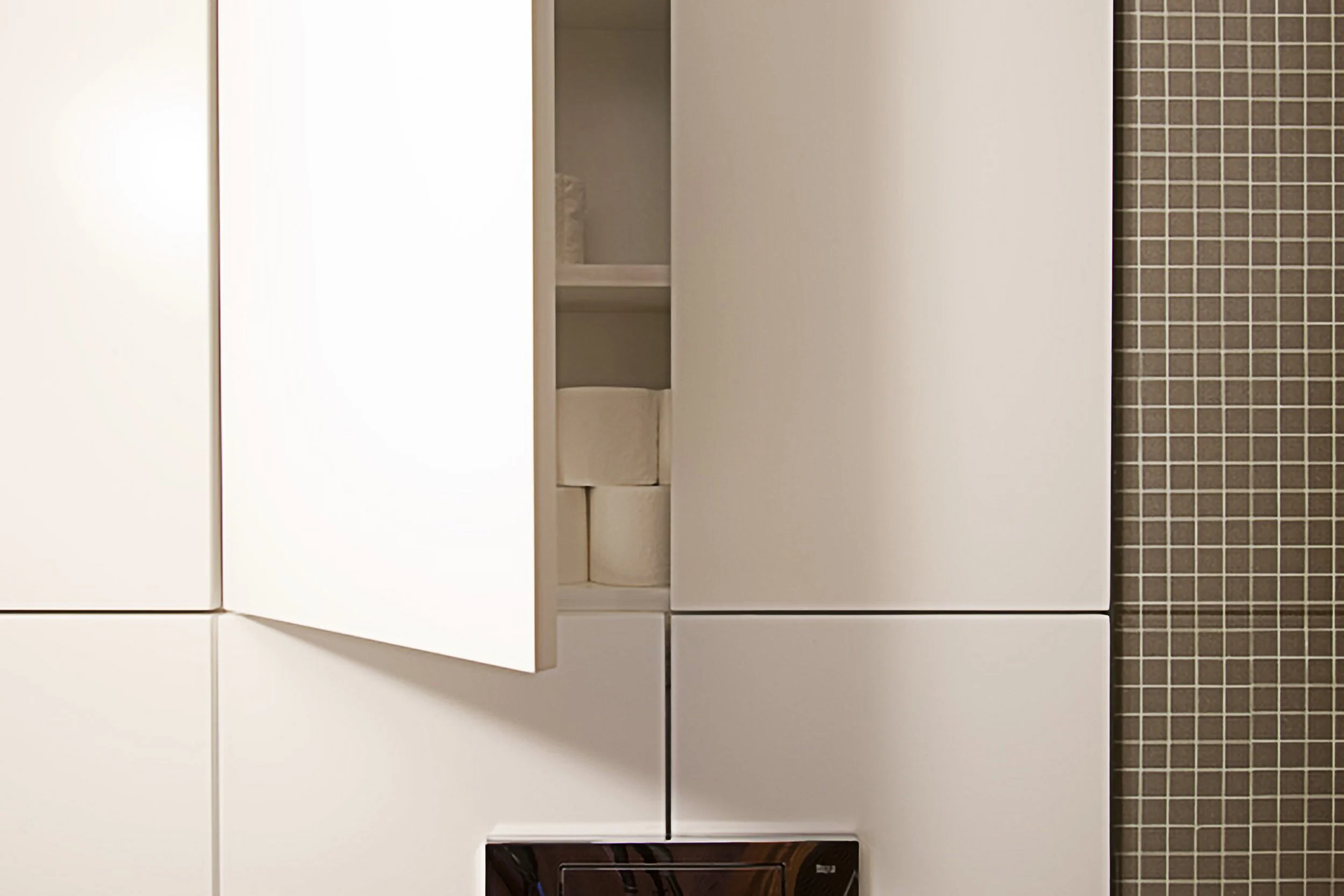 Prateleira com rolos de papel higiênico dentro de um armário branco na cozinha.