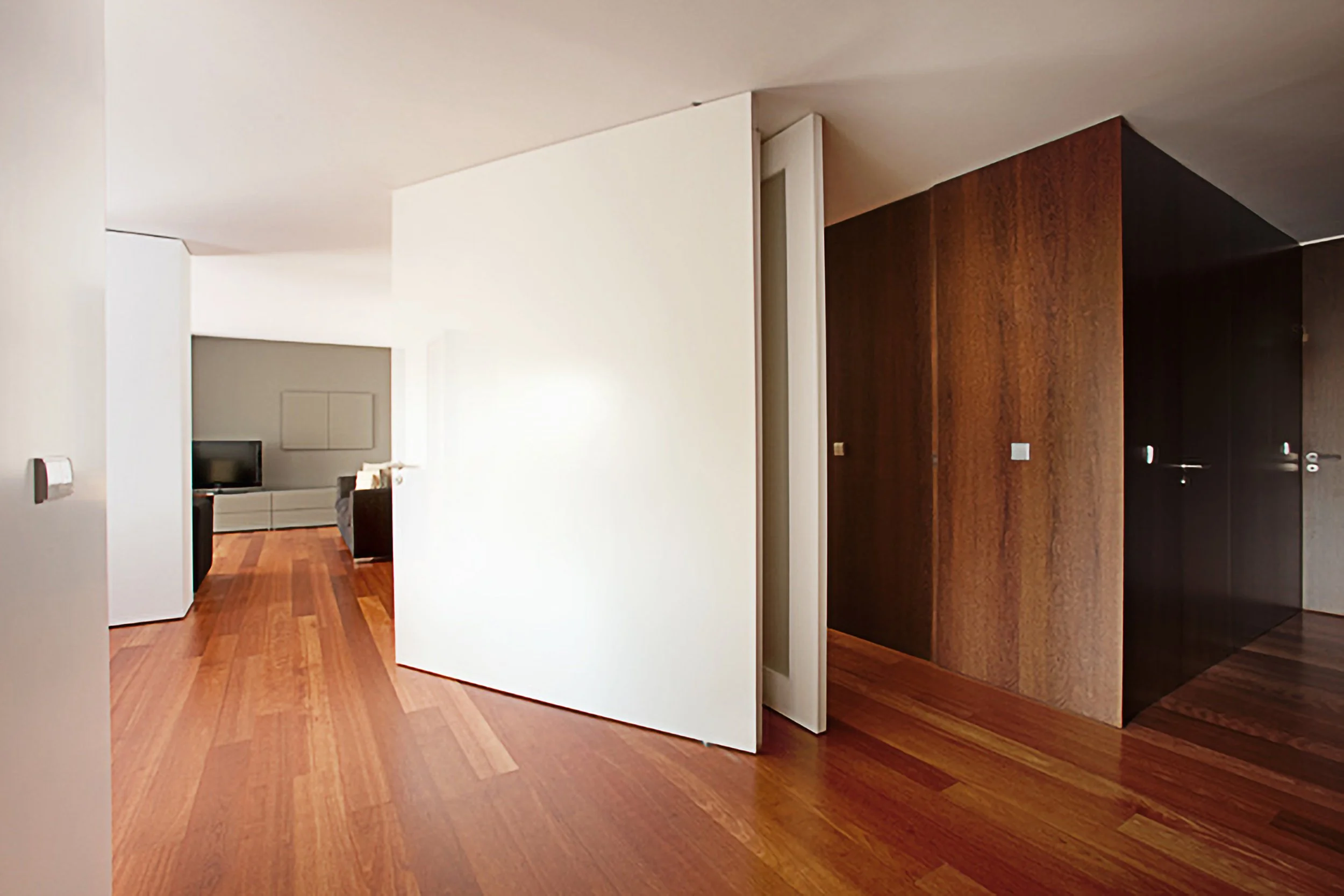 Interior de um apartamento com paredes brancas, piso de madeira e portas de madeira escura.