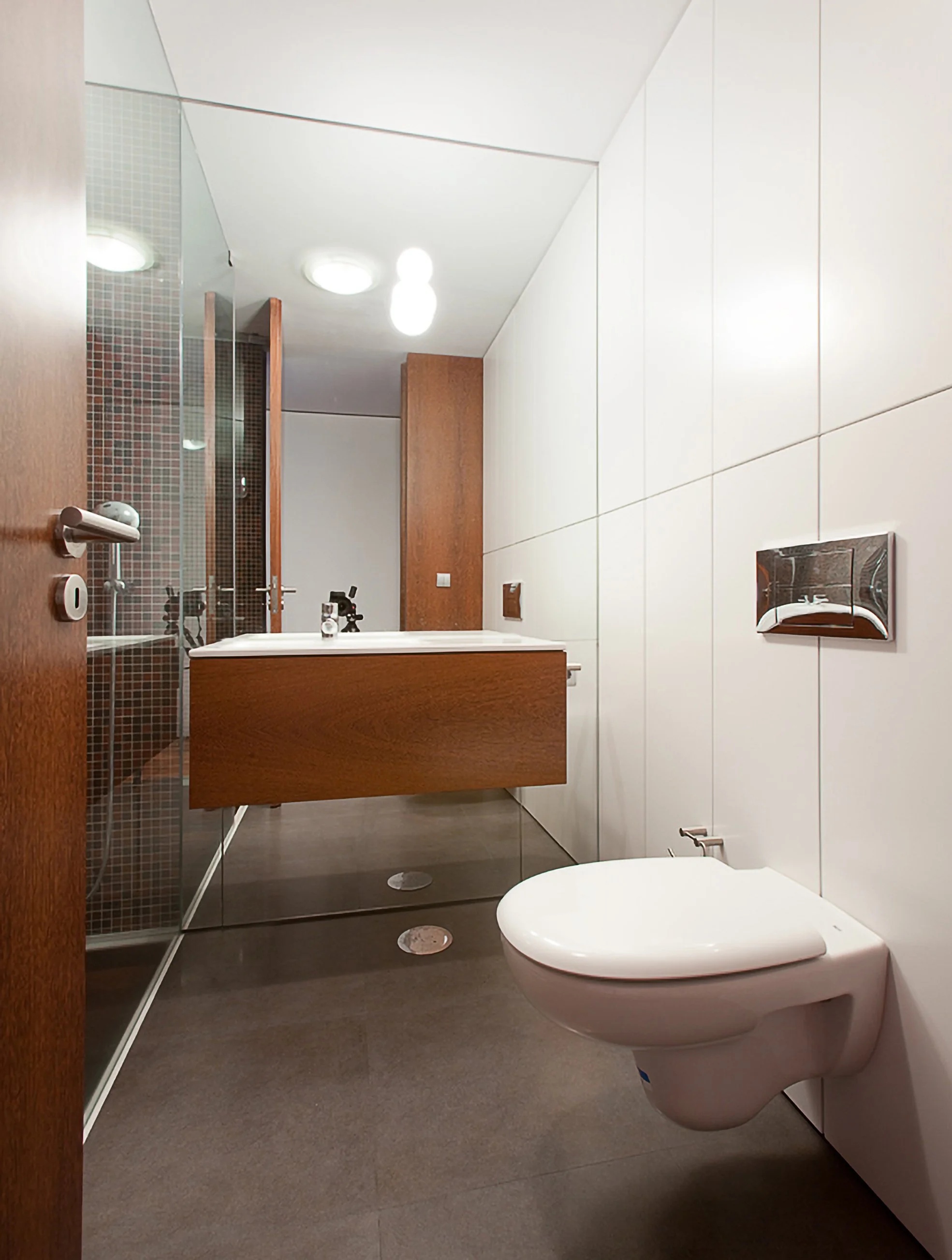 Banheiro moderno com parede de azulejos brancos, vaso sanitário e pia de acabamento em madeira, iluminação luminosa no teto.