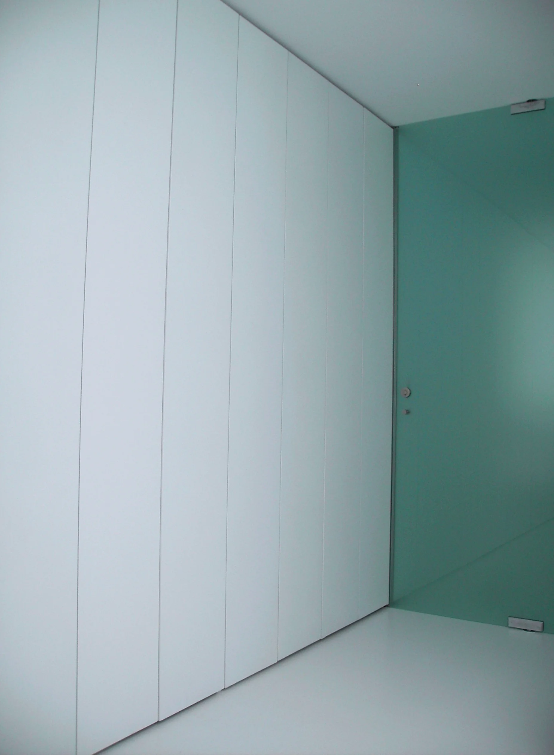 Porta de vidro em um ambiente moderno com paredes brancas e piso branco.