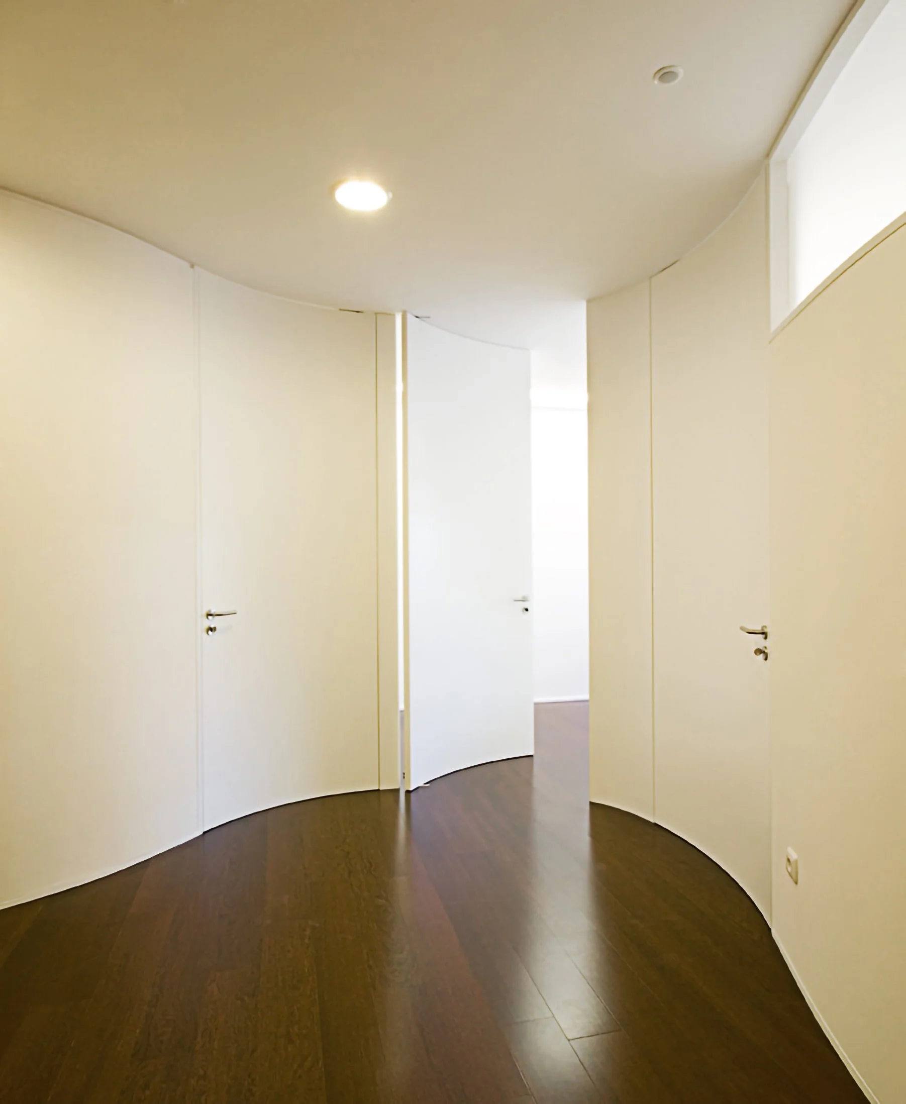 Corredor com portas brancas e piso de madeira escura.