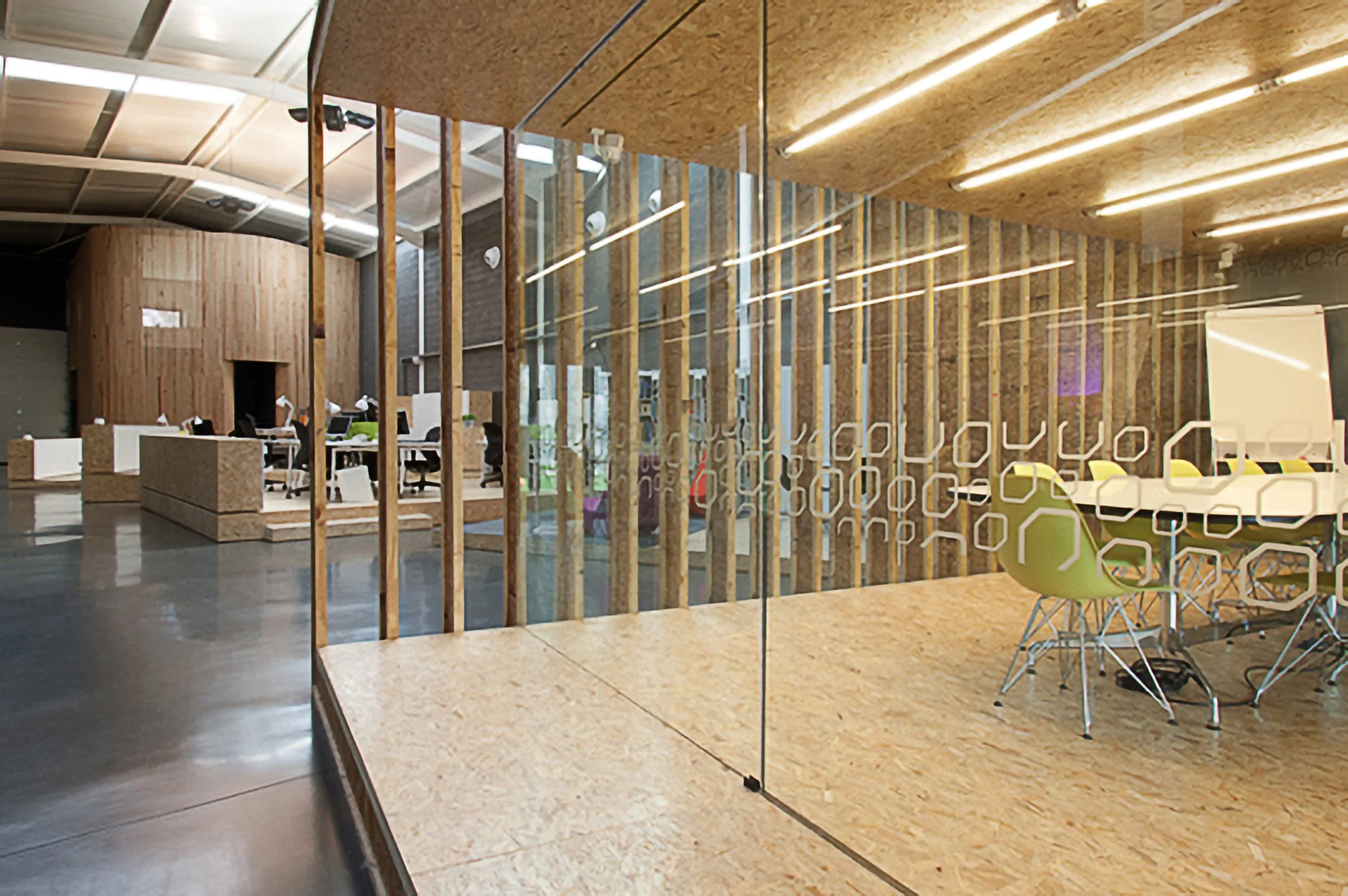 Sala de reunião moderna com mesa, cadeiras verdes e parede de vidro decorada para reuniões de trabalho.