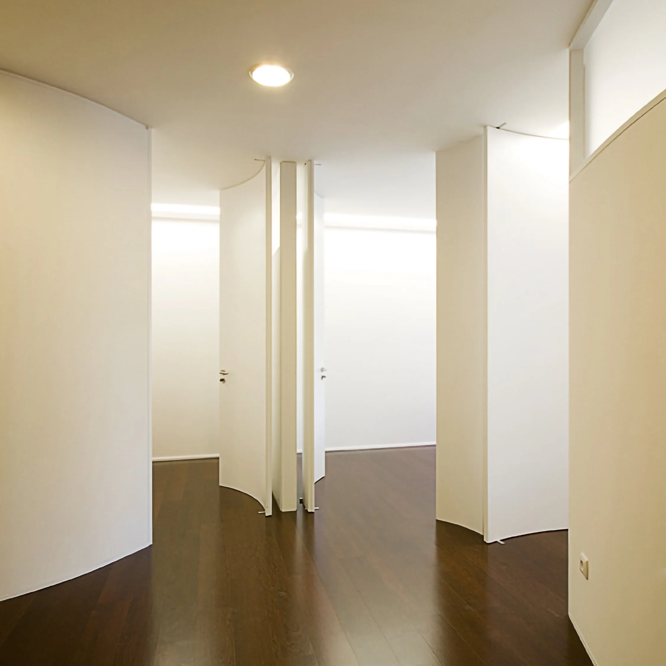 Salas de banheiro com portas curvas brancas e piso de madeira escura.