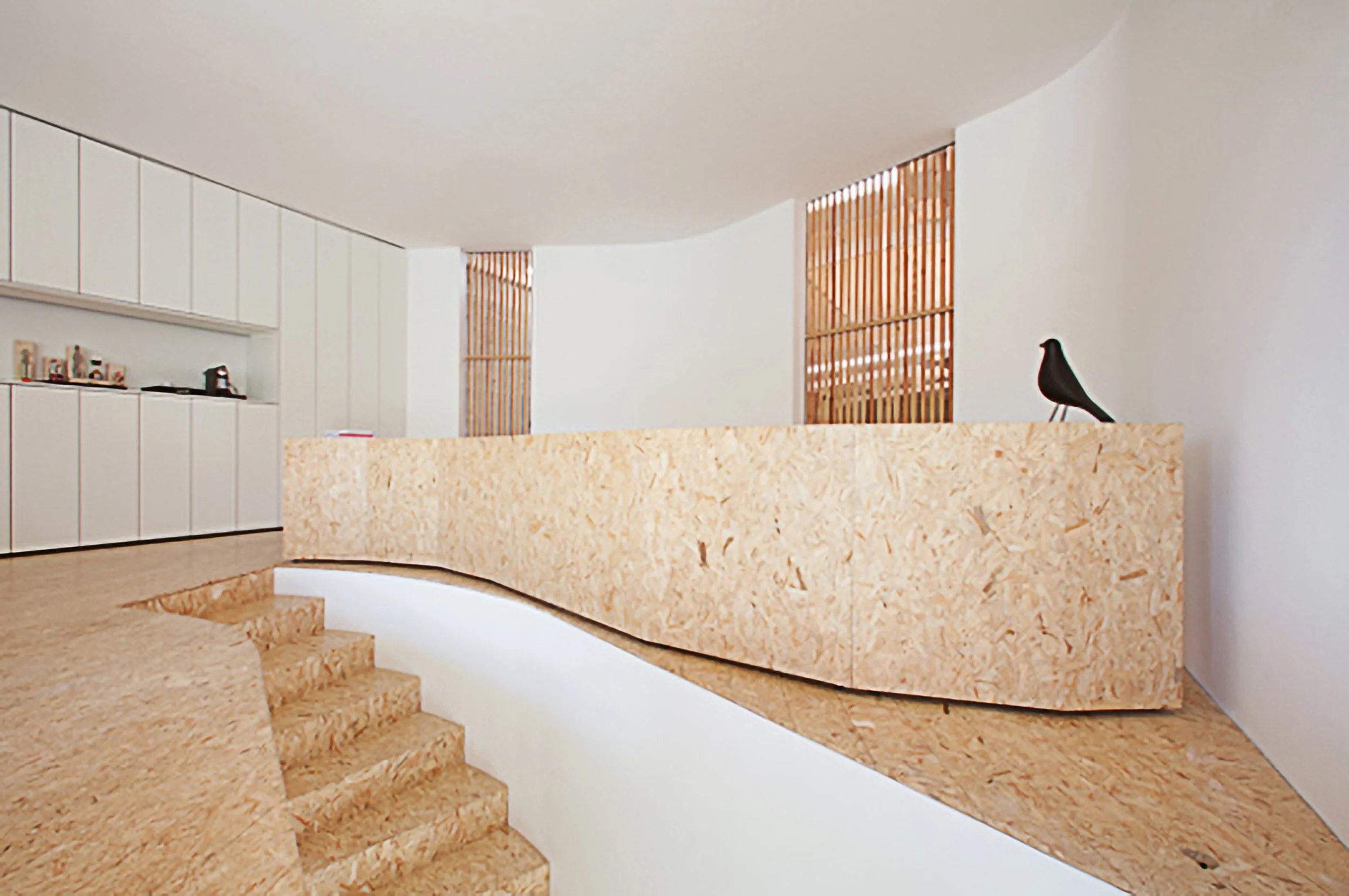 Interior de uma casa moderna com escada de concreto e detalhes em madeira, parede branca, armários brancos e uma decoração minimalista com um pássaro preto de decoração