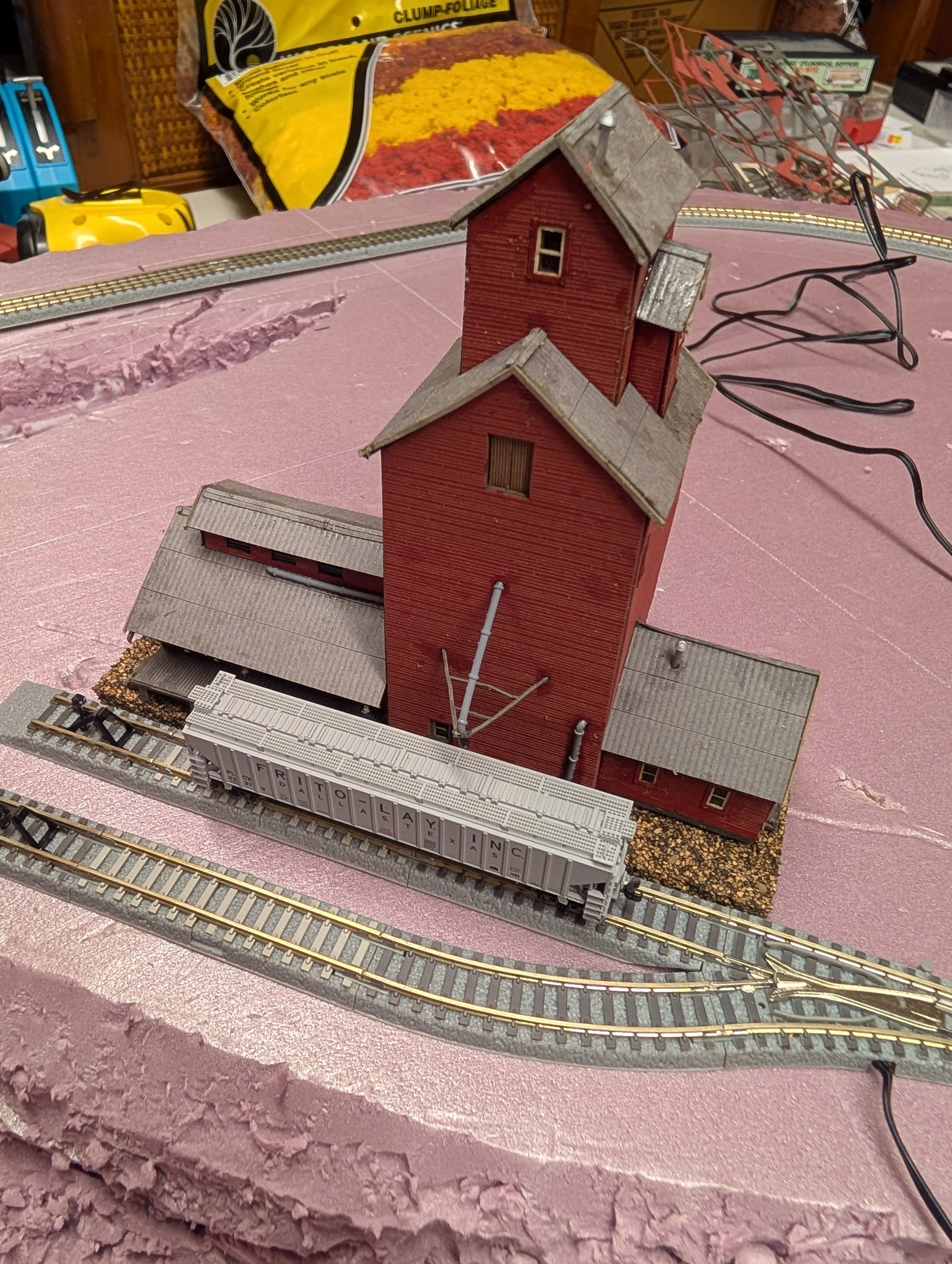 Model railroad scene with red grain elevator, train tracks, and a freight train car spelling out "FREIGHTLAYING" on a foam base.