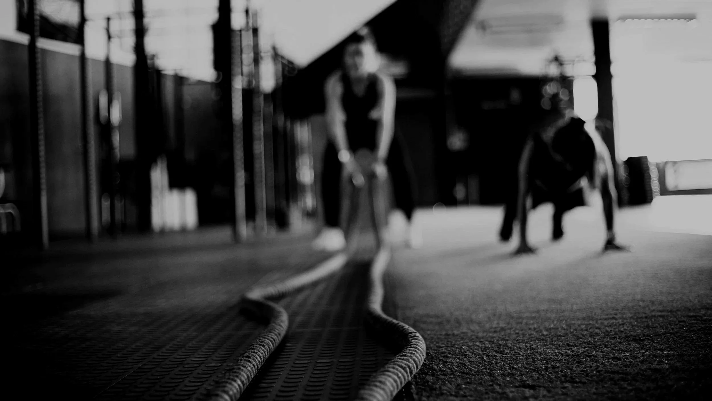 Black-and-white photo of two firefighters in uniform entering a building with a hose laid out on the floor.