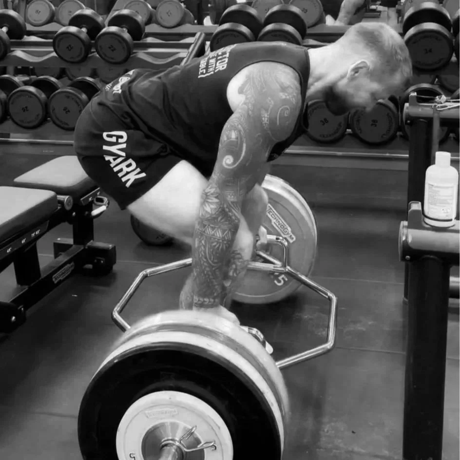 A man with tattoos lifting a barbell with weights at a gym.
