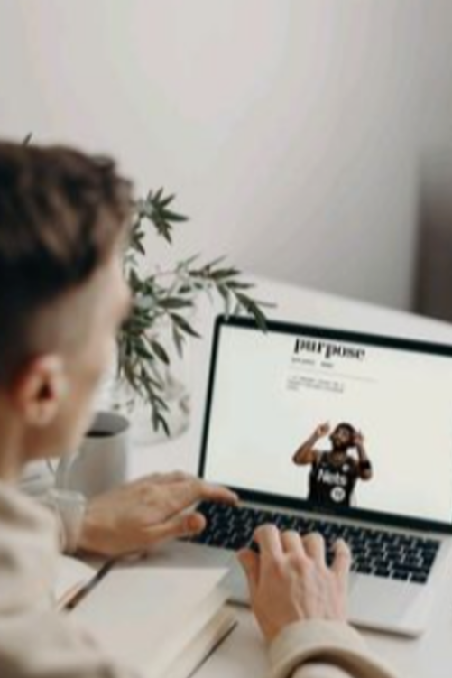 Person browsing a website on a laptop in a bright room with a plant in the background.