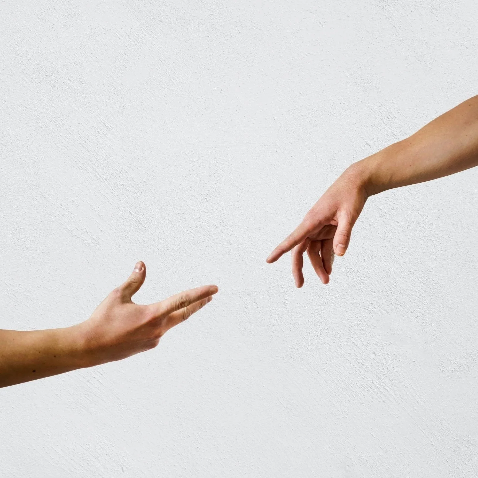 Two hands reaching towards each other against a white textured wall background.
