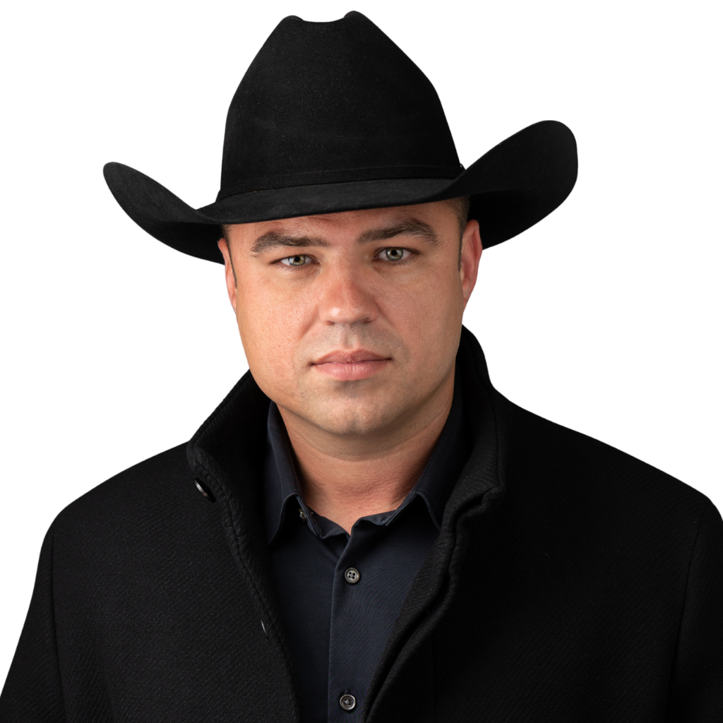 Nathanael Schultz wearing a black cowboy hat, black jacket, and dark shirt, looking directly at the camera with a serious expression.