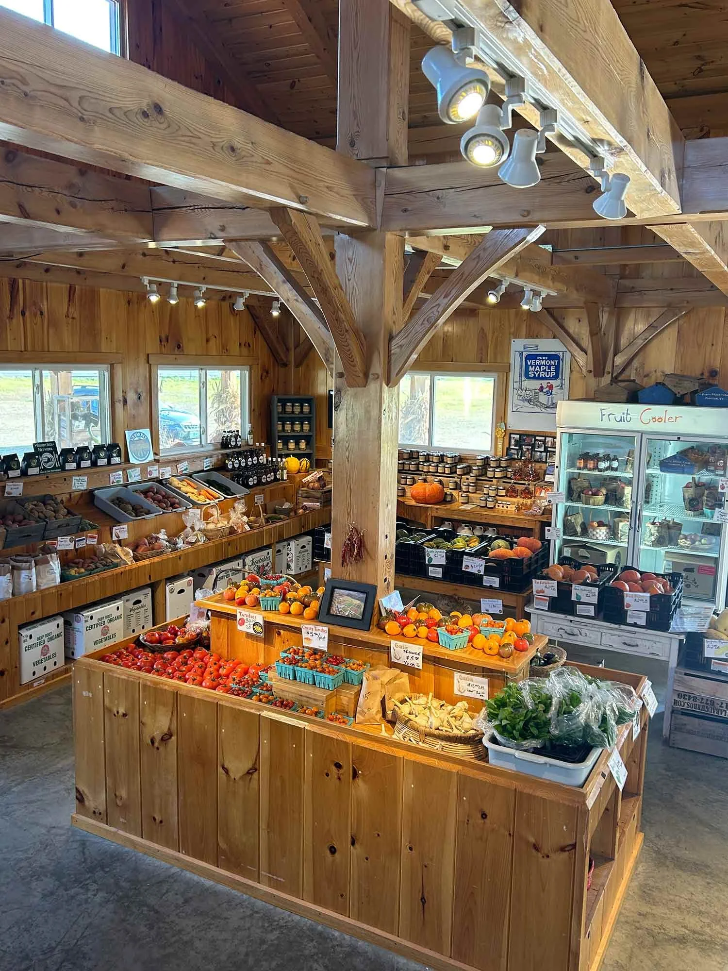 Inside the Foote Brook Farm Store with wooden beams and walls, displaying fresh fruits and vegetables like tomatoes, pumpkins, and leafy greens.