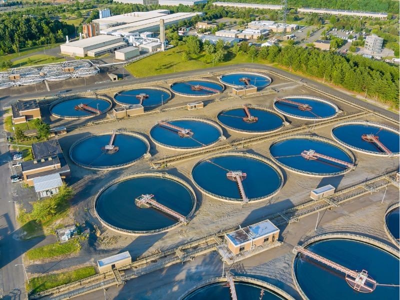 Estação de tratamento de água com tanques circulares de lavagem, ao fundo áreas industriais e vegetação.
