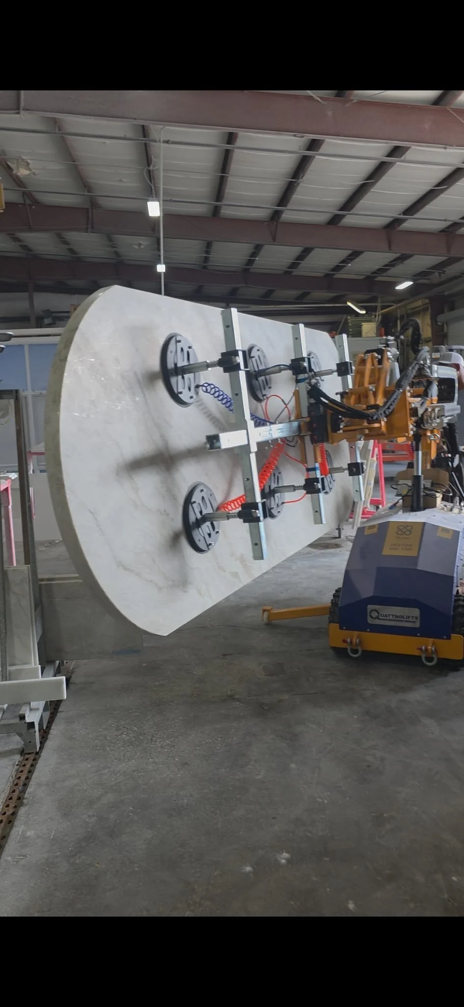 A hydraulic lift machine holding a large marble or stone slab in an industrial workshop or warehouse. Lift Operator.