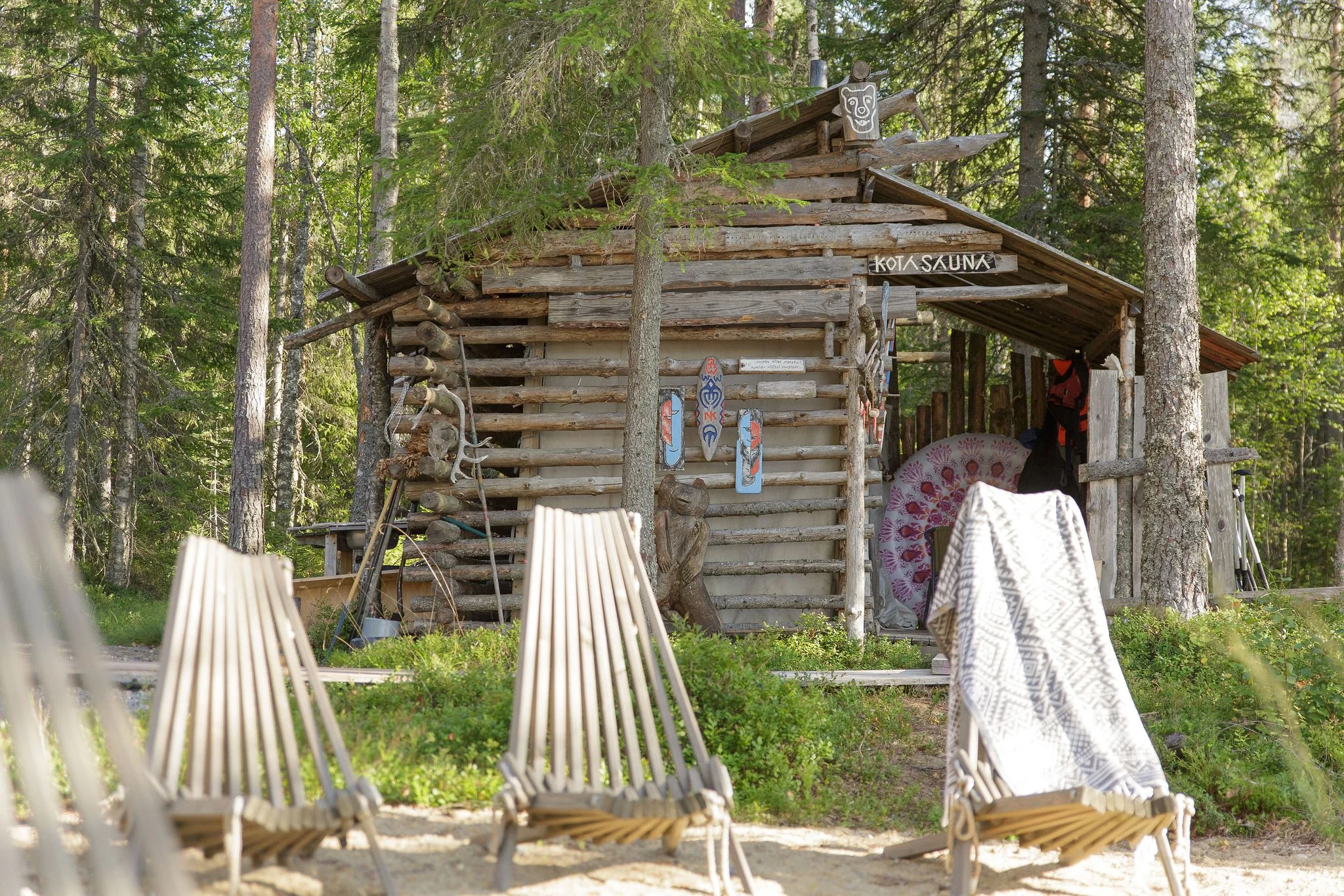 Saunamaailman telttasauna metsän keskellä ja sen edustalla puisia aurinkotuoleja.