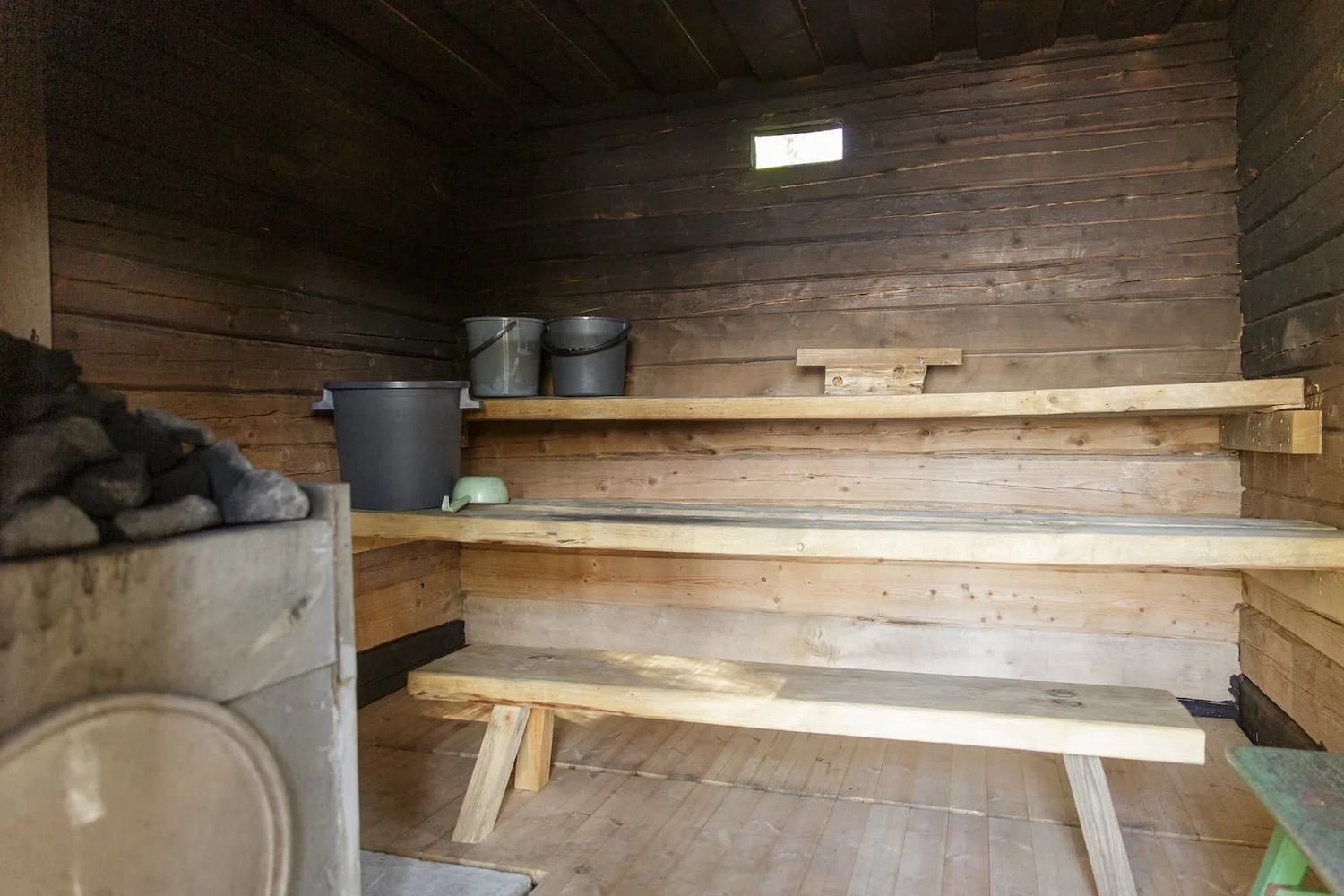 Wooden sauna room with a bench, buckets, and a stove with rocks.
