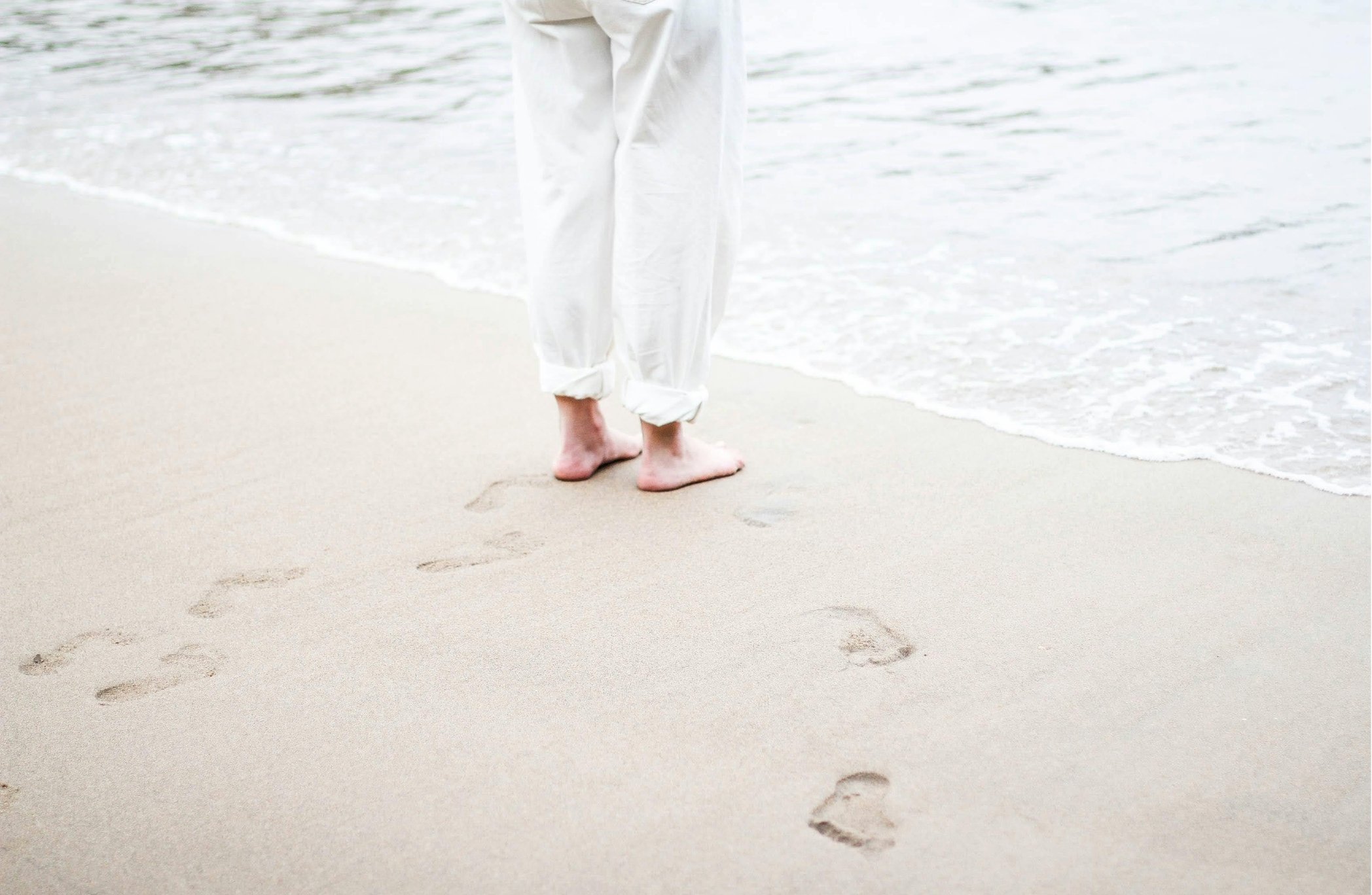 Person walking along the beach, leaving footprints in the sand with the ocean waves nearby.