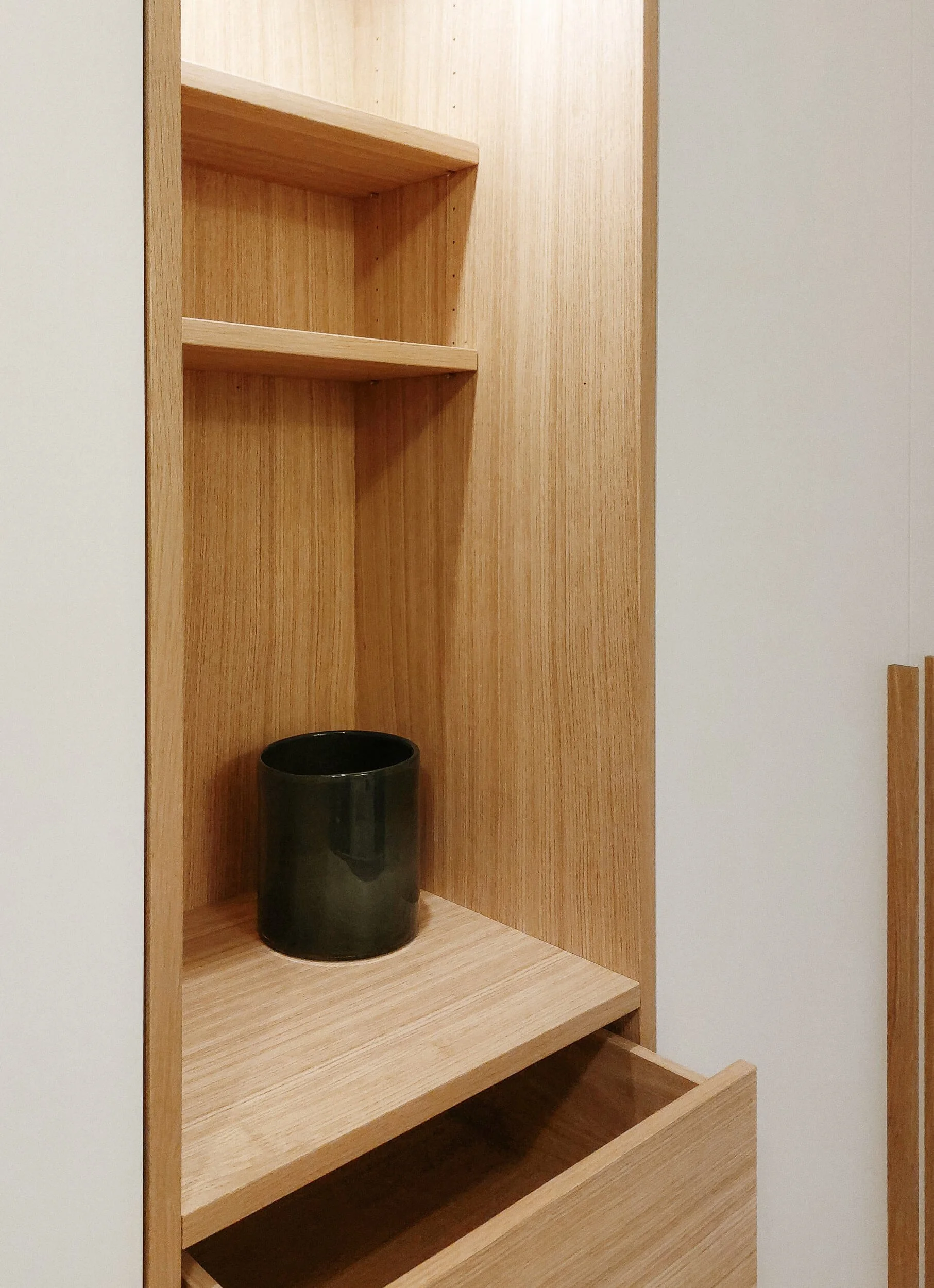 Ein Holzregal mit mehreren offenen Fächern, darin eine schwarze Keramiktasse auf der unteren Ablage