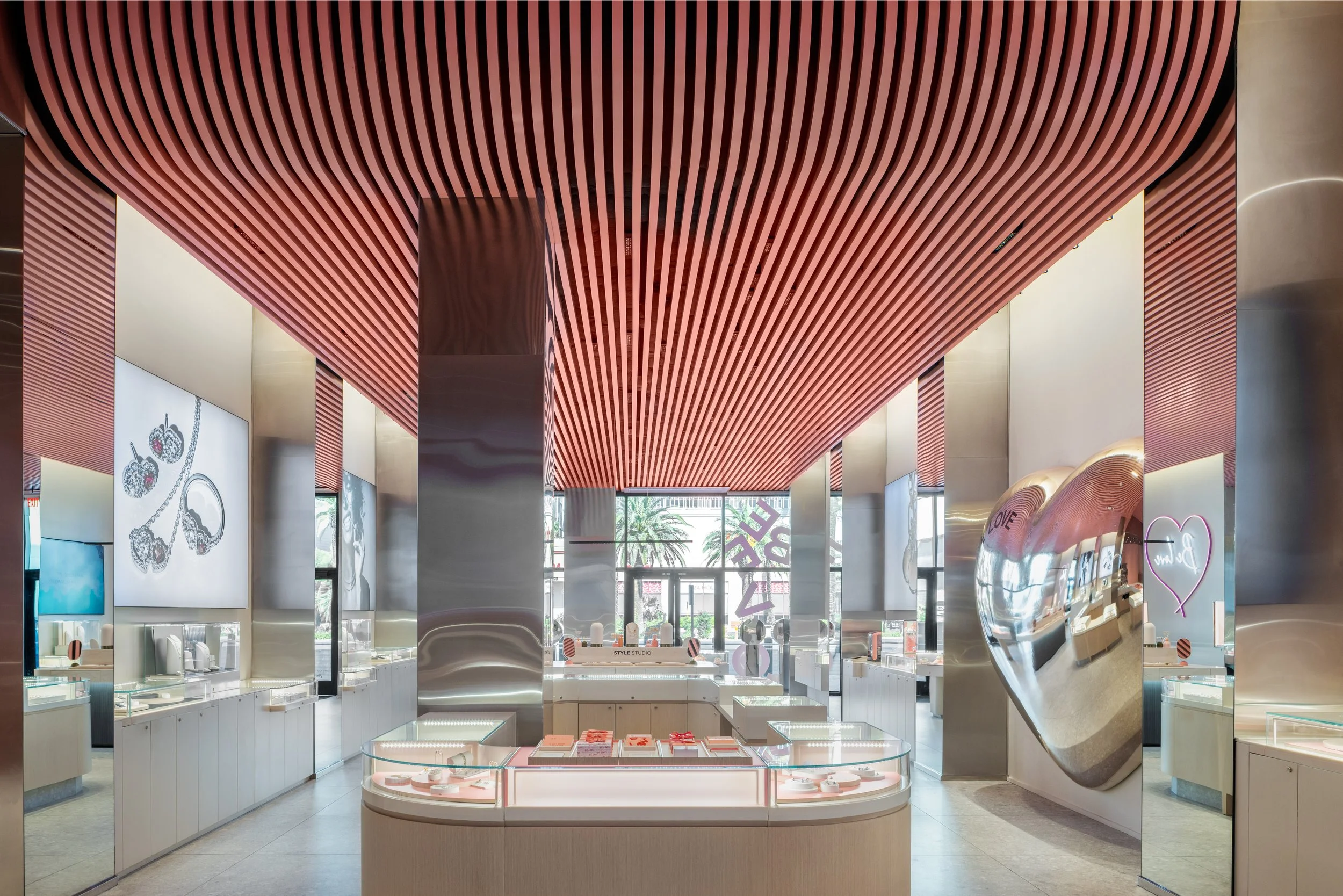 Interior view of a jewelry store with pink ceiling slats, mirrored walls, and display cases showcasing jewelry.