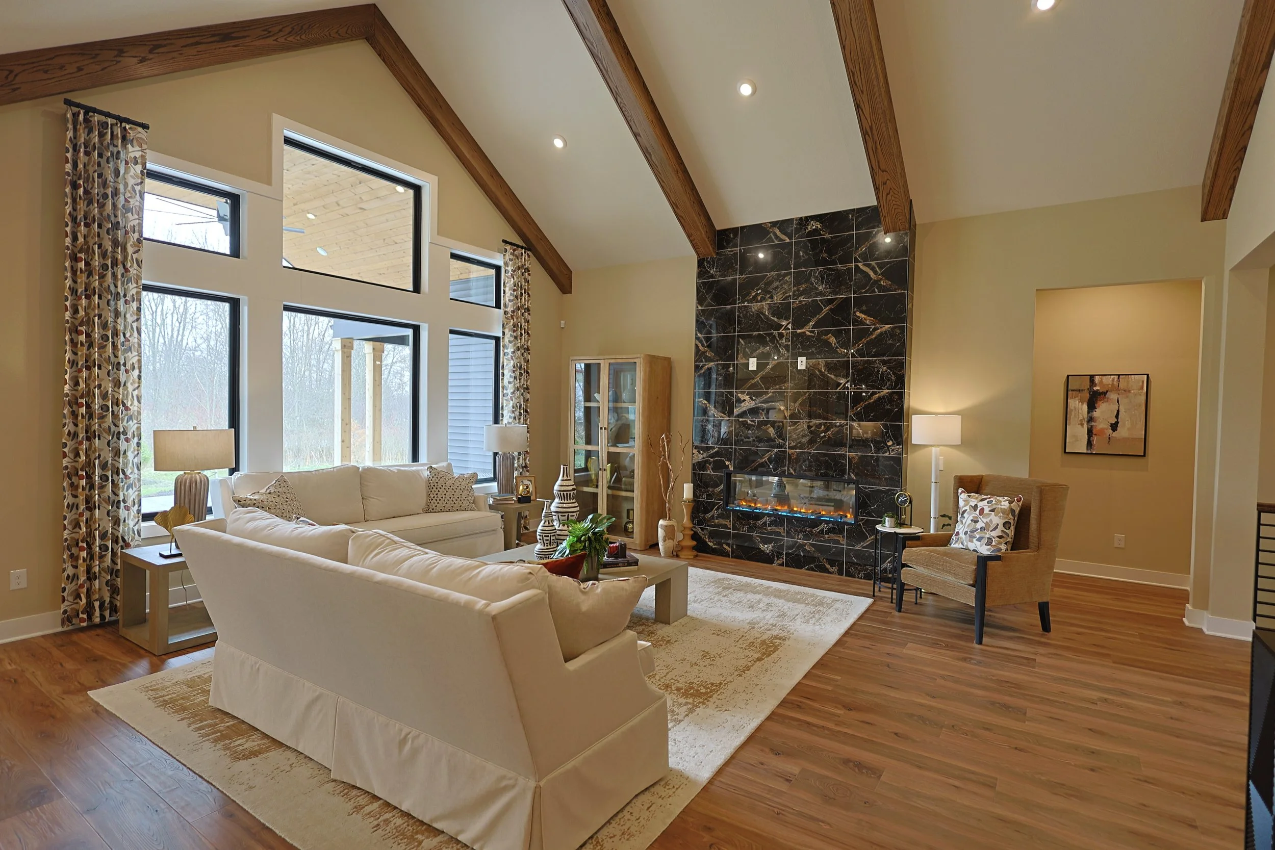 Spacious living room with large windows, white sofas, a wood fireplace framed by black marble, and hardwood floors.