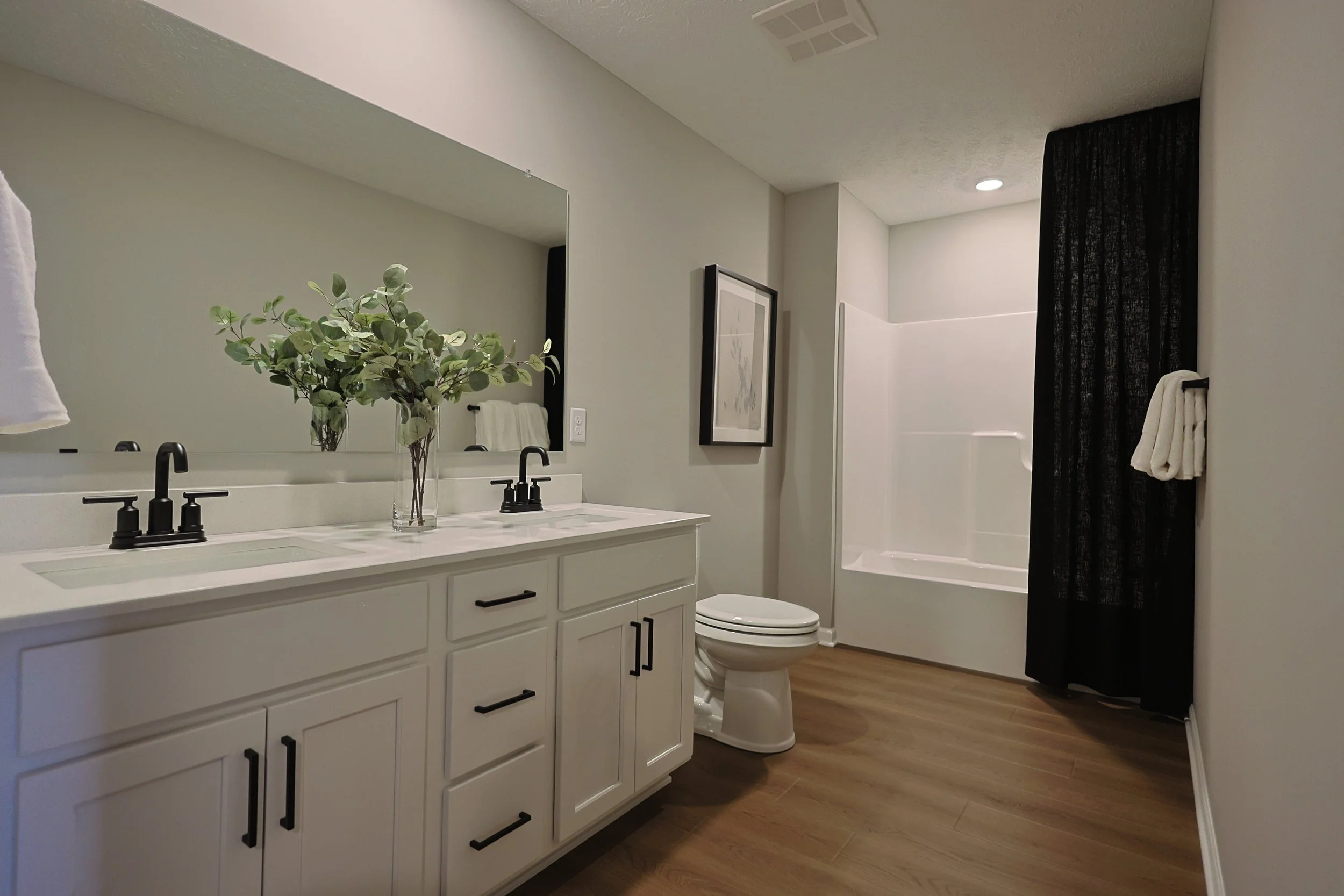 Modern bathroom with double vanity, large mirror, framed art, and walk-in shower with black curtain.