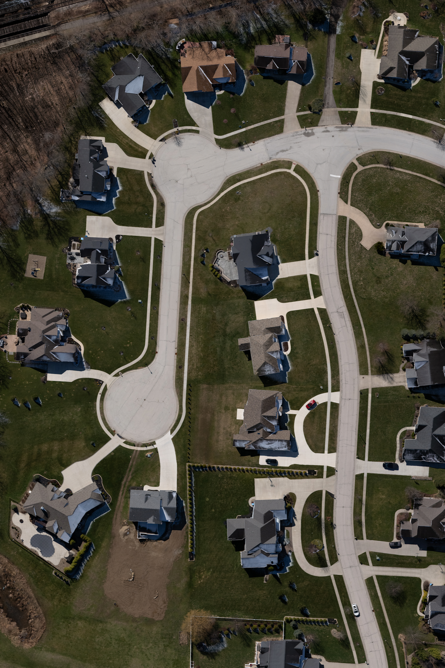 Aerial view of a suburban neighborhood showing houses, grass lawns, paved driveways, and a network of empty concrete streets with cul-de-sacs.