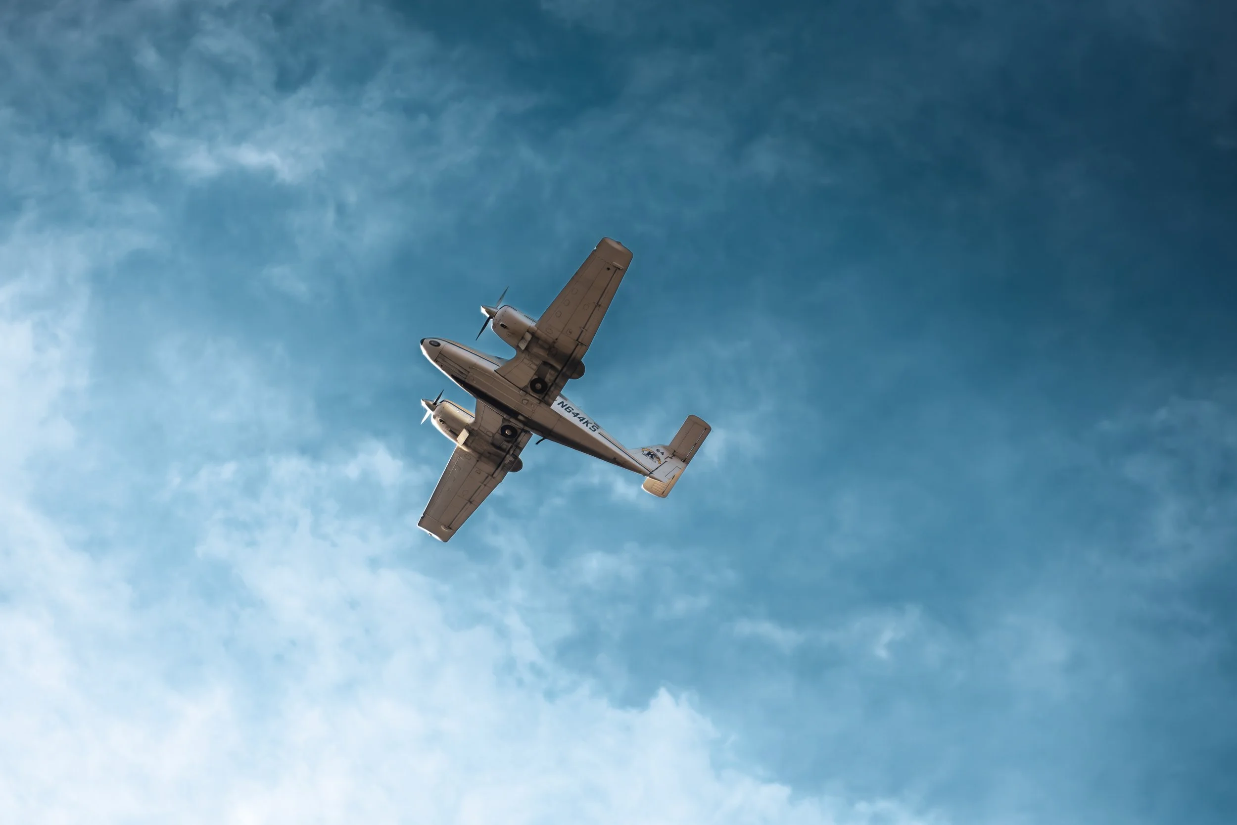 A twin-engine propeller airplane flying in a blue sky with scattered clouds.