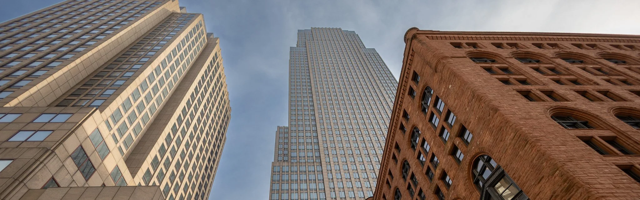 Low-angle view of three tall buildings with a blue sky background, showcasing architectural details of modern and historic skyscrapers.