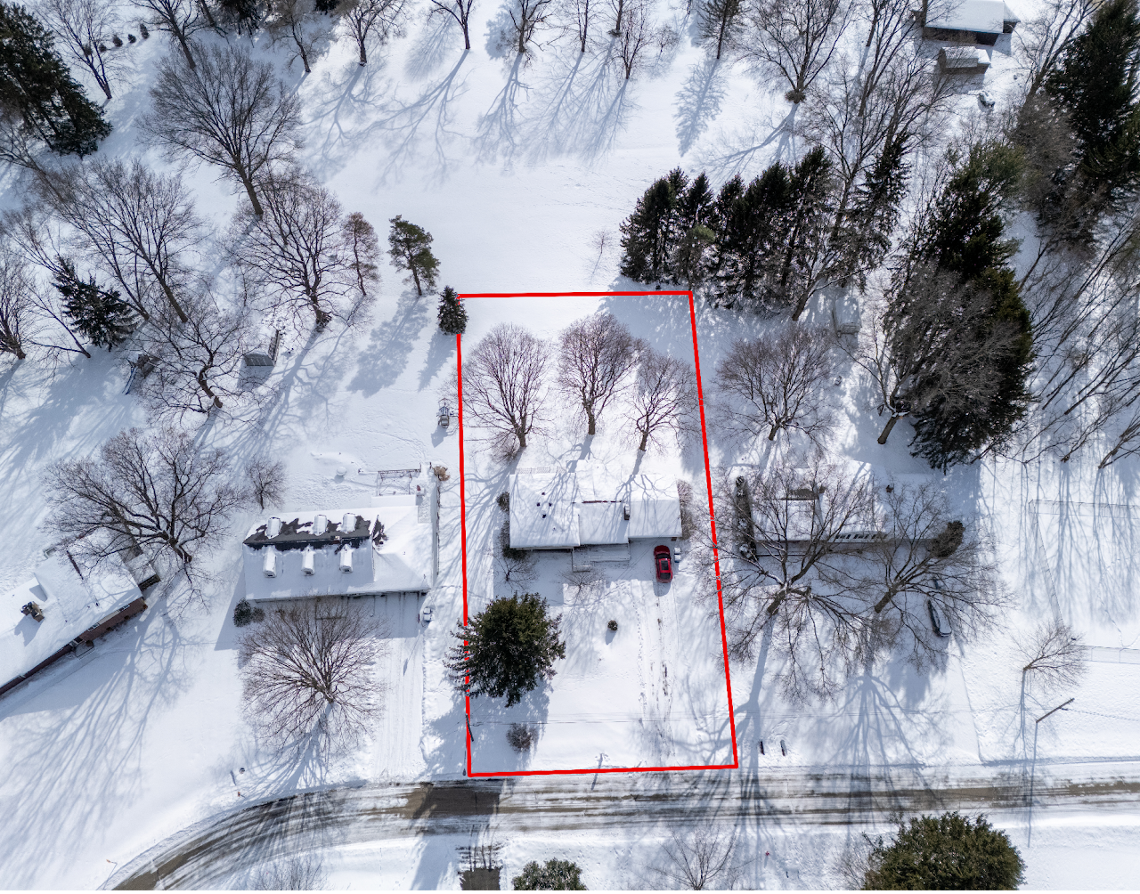 An aerial view of a snow-covered residential property with a house, trees, and a driveway, outlined in red for property boundaries.
