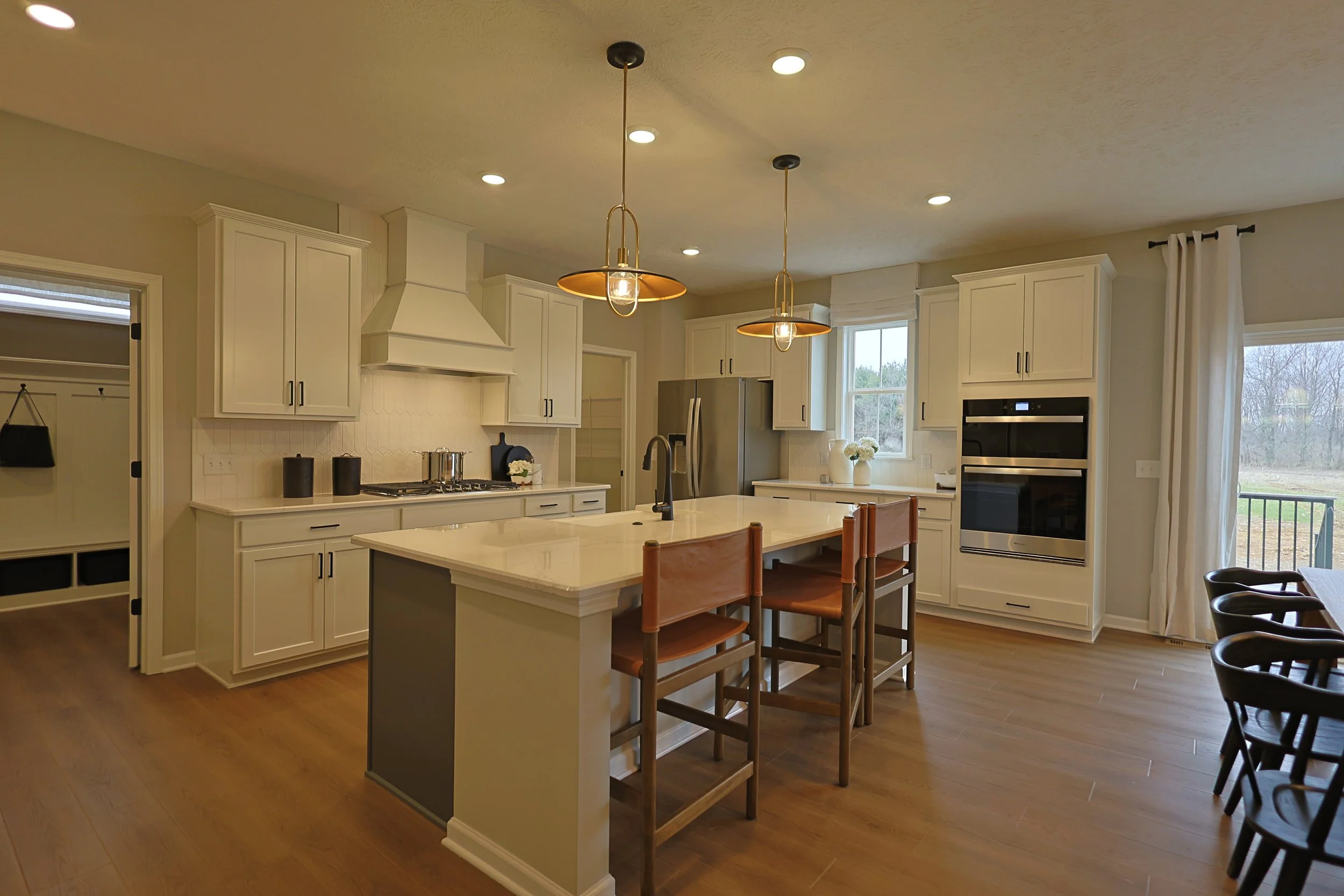A modern kitchen with white cabinets, a large island with a beige countertop, pendant lights, stainless steel appliances, and hardwood flooring.