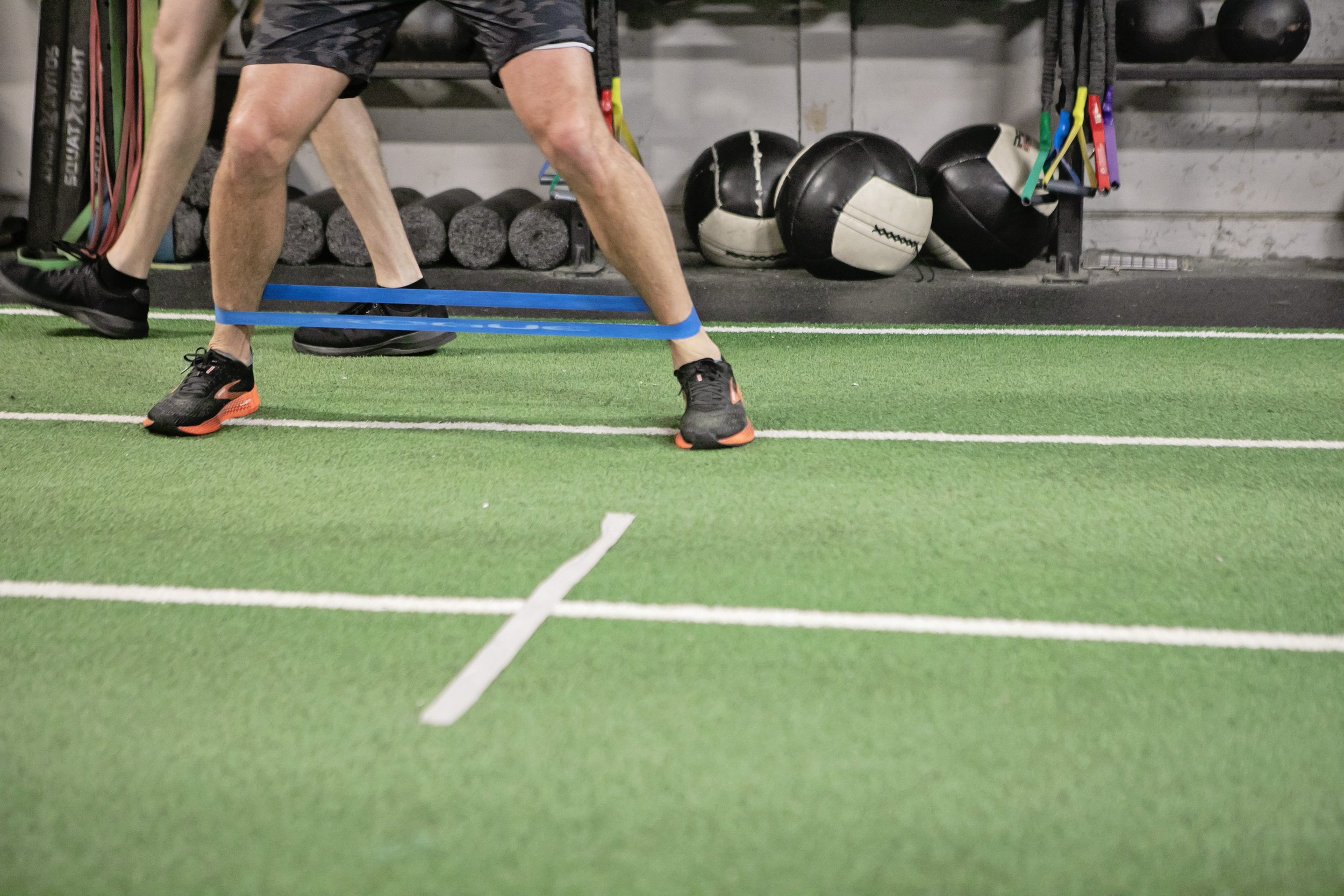 Person exercising with resistance band on synthetic turf in the Edge Performance Valdosta gym.