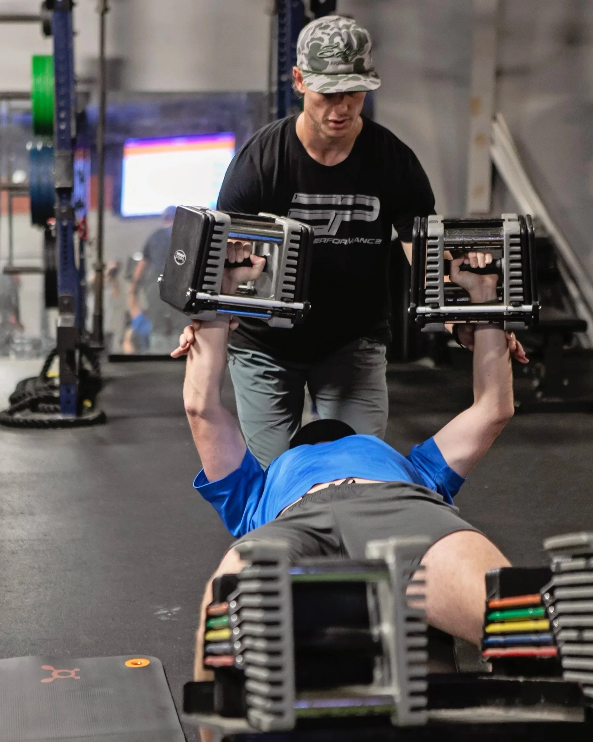 Austin Grant, founder and training director at Edge Performance in Valdosta, assists a member with a dumbbell chest press inside the gym.