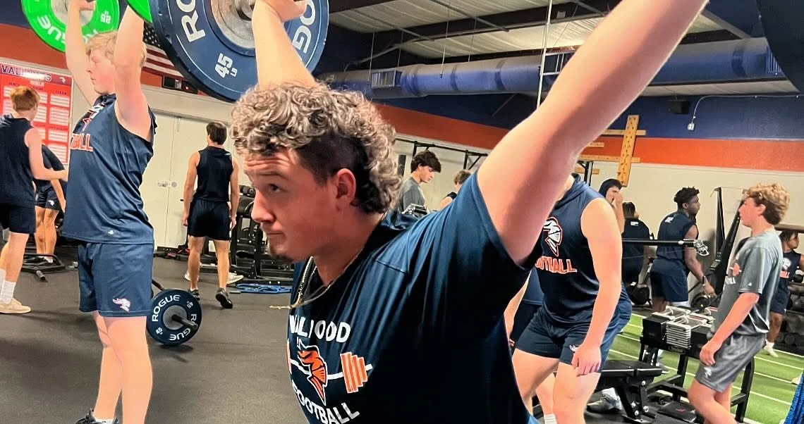 Young athletes working out in the Edge Performance Valdosta gym. One person is lifting a barbell overhead, and others are doing various exercises.