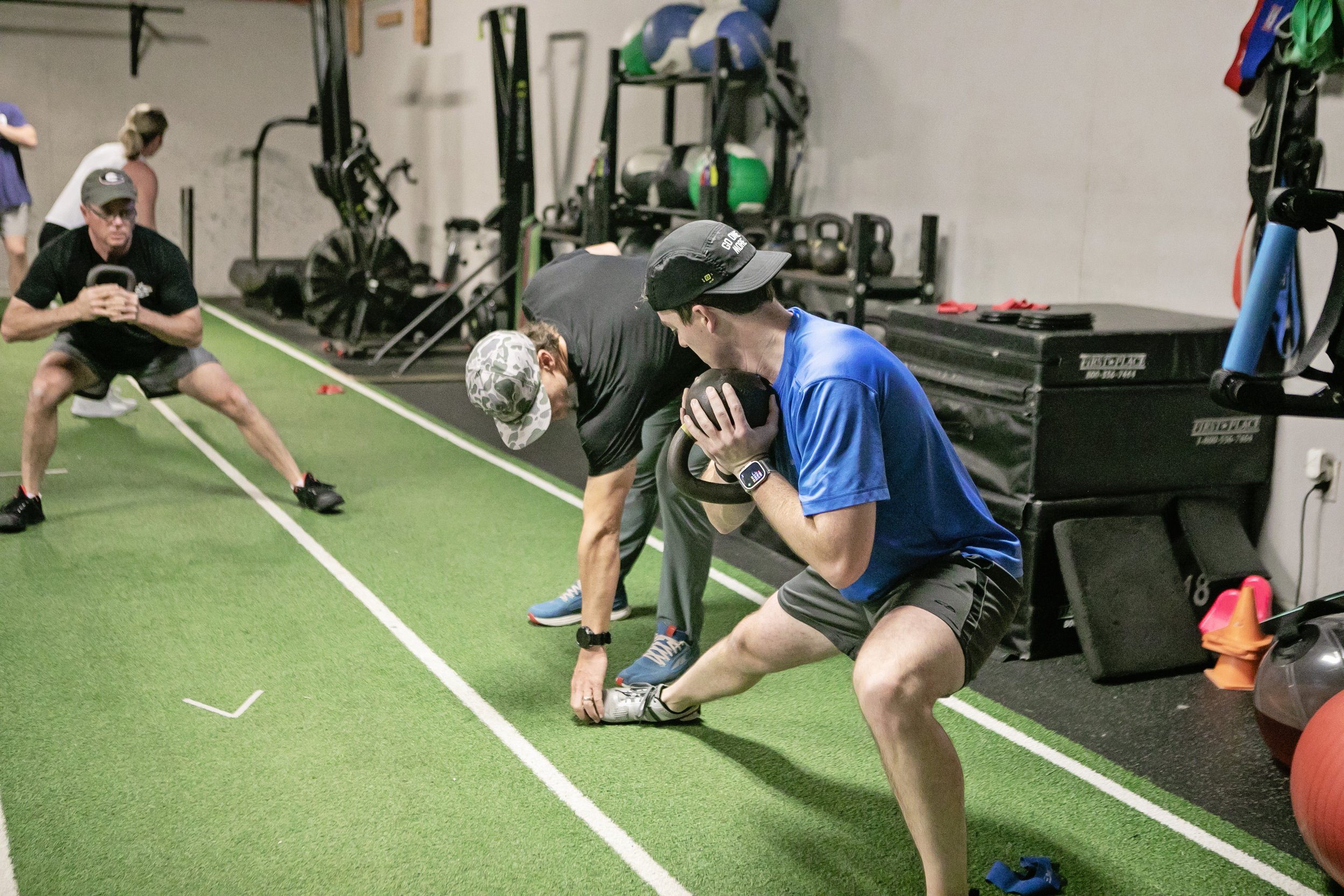 A trainer giving instructions to a gym member on a turfed workout area at Edge Performance Valdosta.