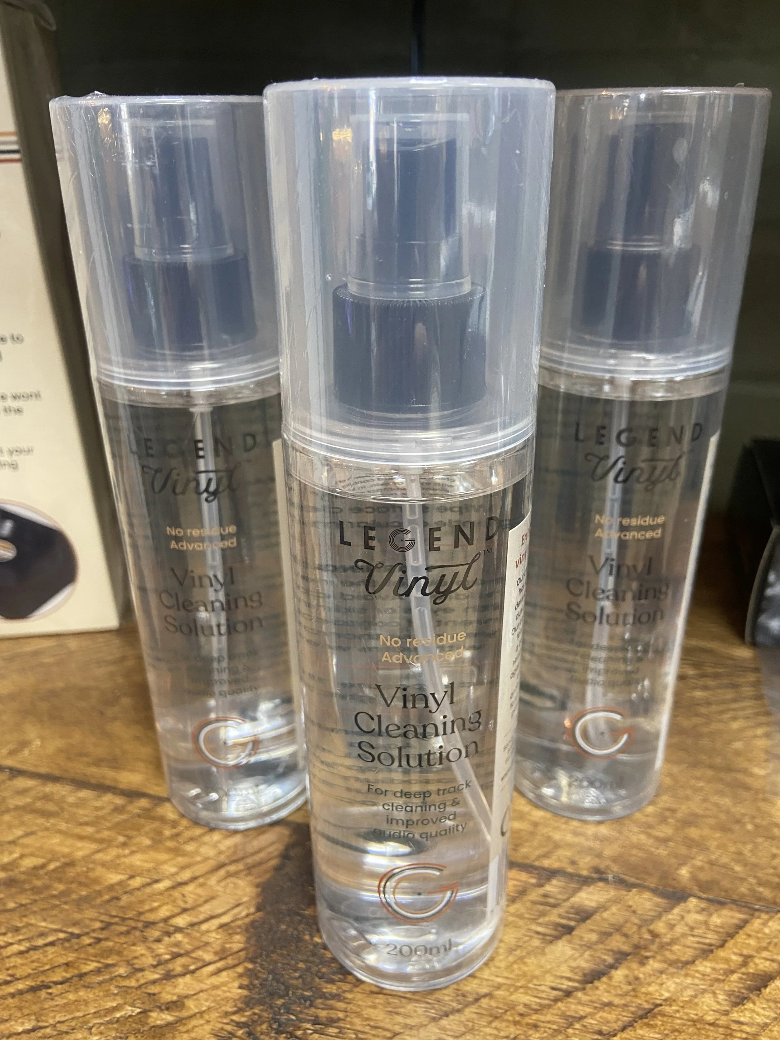 Four clear cylindrical spray bottles of vinyl cleaning solution with black spray nozzles, labeled 'Vinyl Cleaning Solution' on a wooden surface.