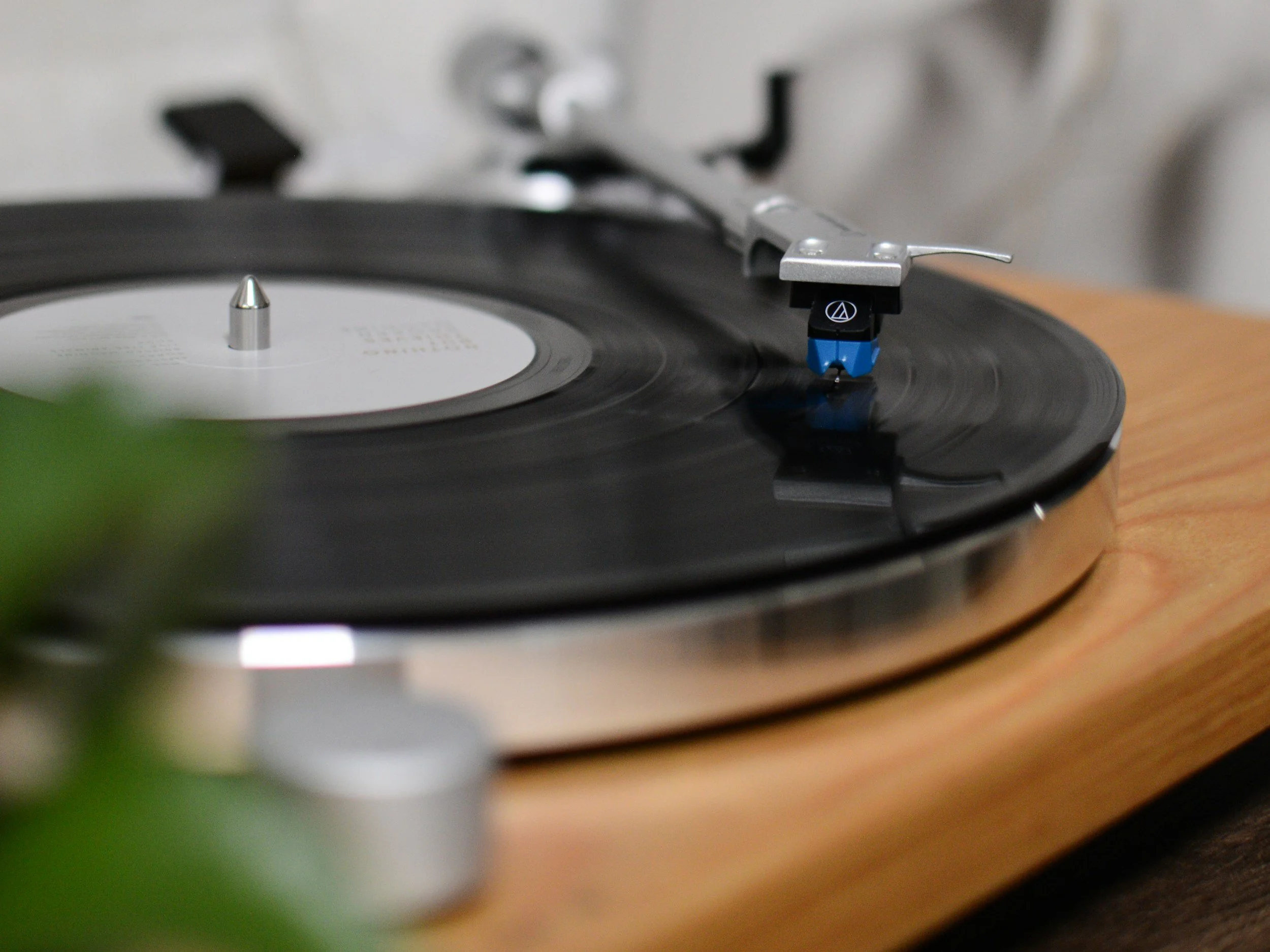 Close-up photo of a vinyl record spinning on a turntable, with the record's label visible and the tonearm positioned over it.