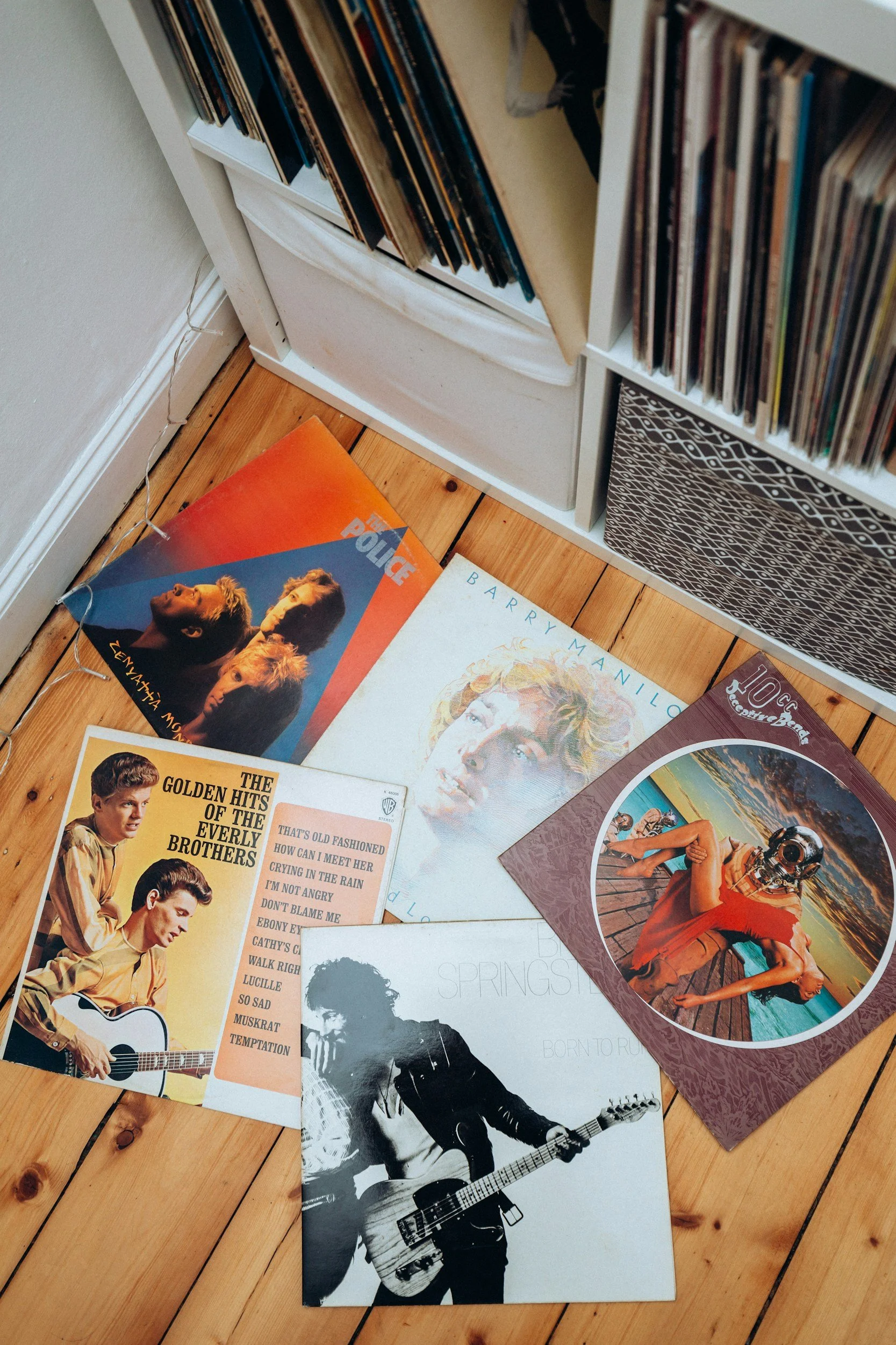A vinyl record collection with album covers laying on a wooden floor, featuring artists like The Everly Brothers, Barbra Streisand, and The Beatles.