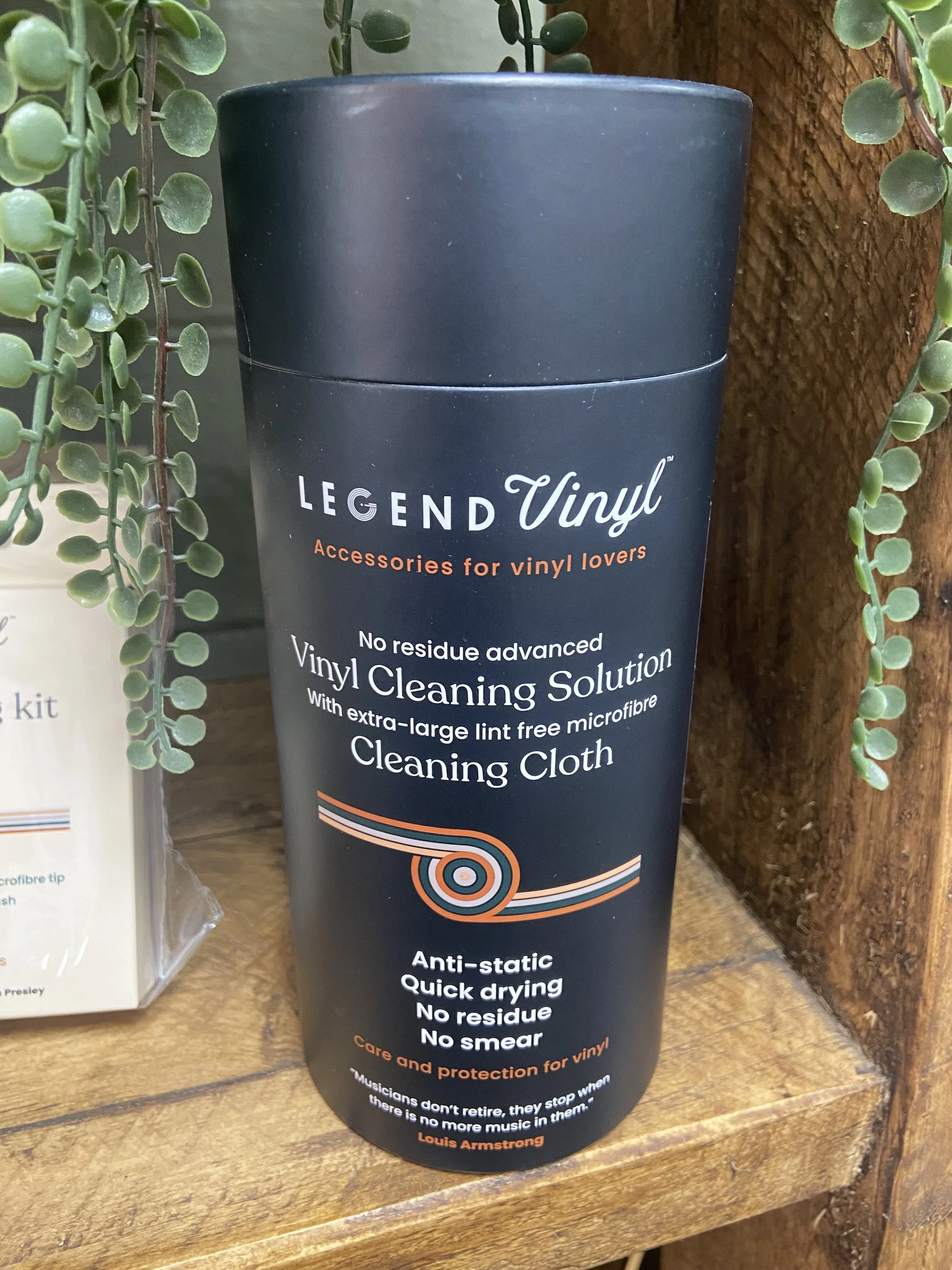 Black cylindrical container of Vinyl Cleaning Solution surrounded by green plants on a wooden surface.