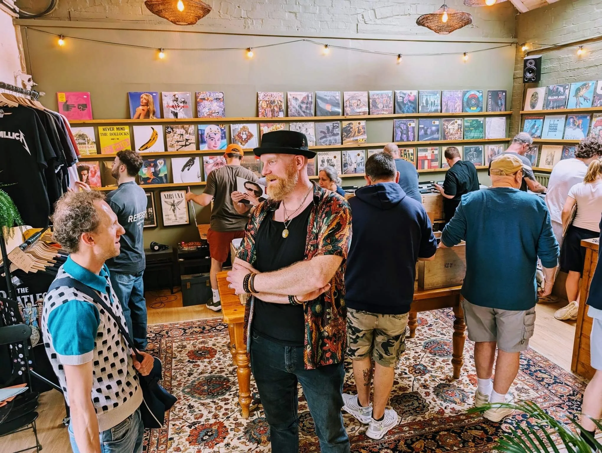 A group of people browsing vinyl records in a store decorated with string lights and framed artwork on the wall.