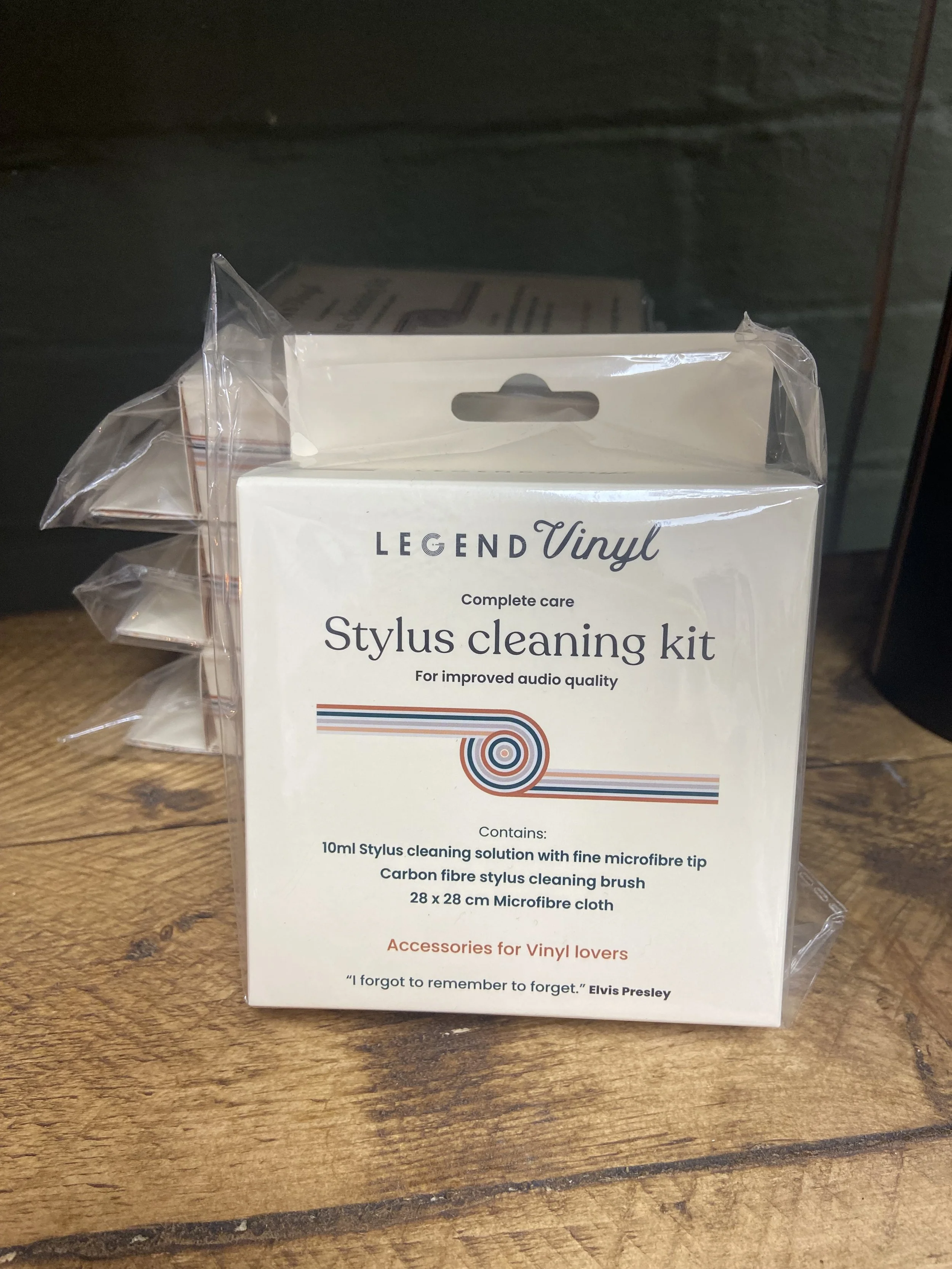 Packaging box for a vinyl stylus cleaning kit, placed on a wooden surface. The box is predominantly white with some colorful lines and text describing its contents and purpose.