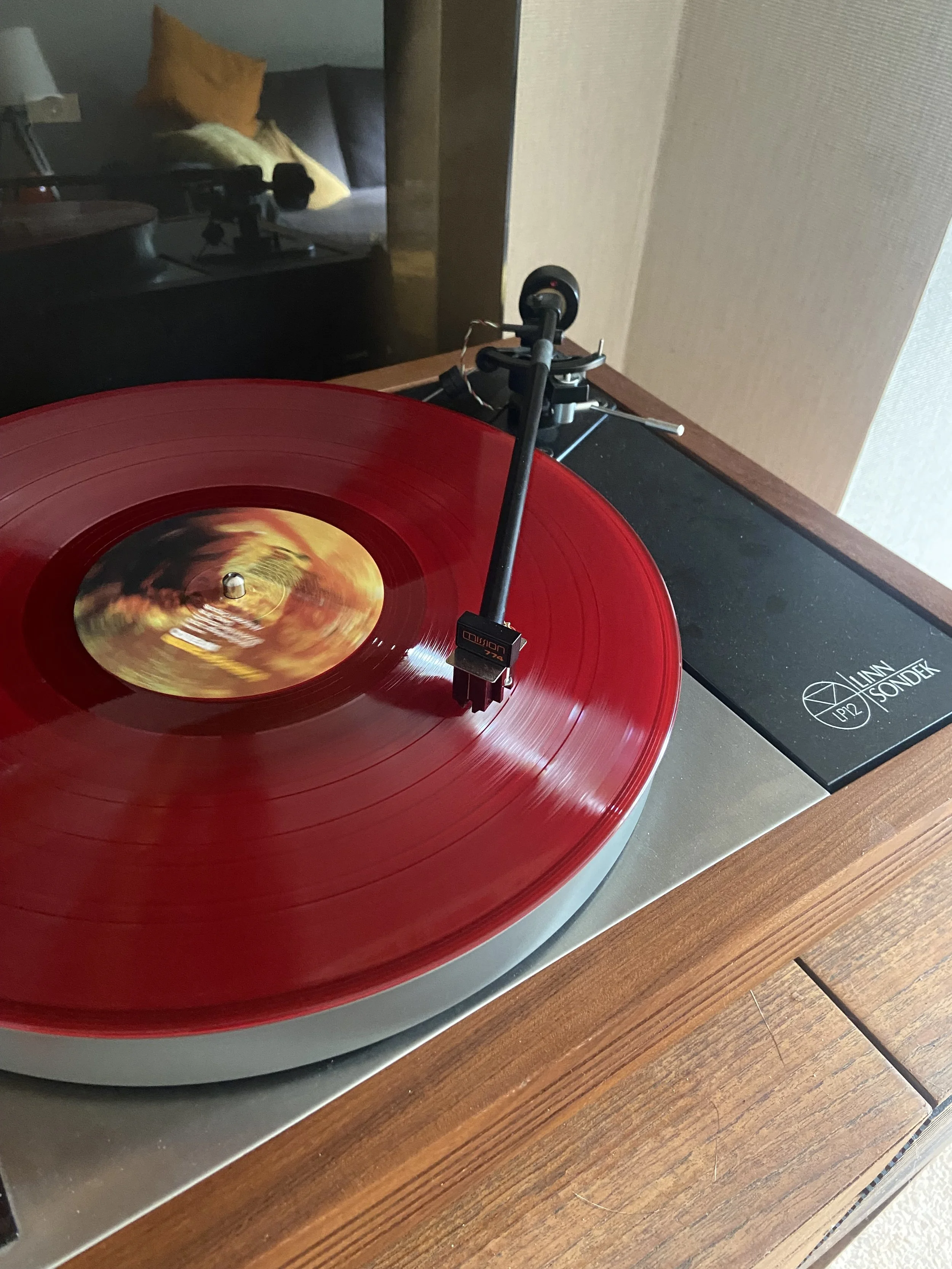 A red vinyl record spinning on a turntable in a room with a bed and pillows visible in the background