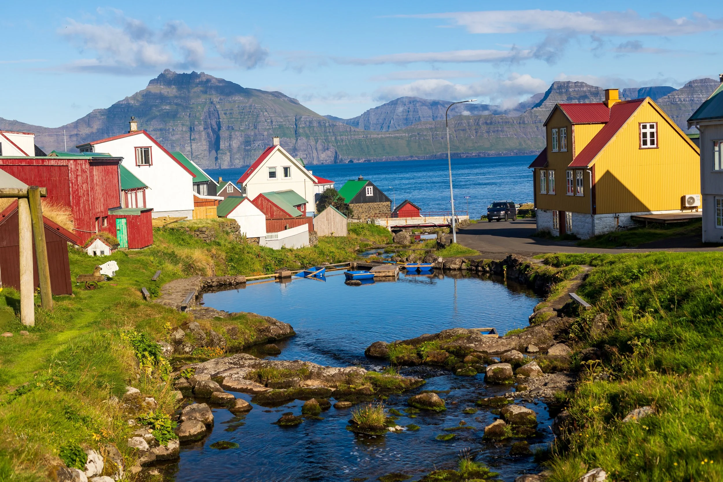 Colorful houses near a small creek with mountains in the background under a blue sky.