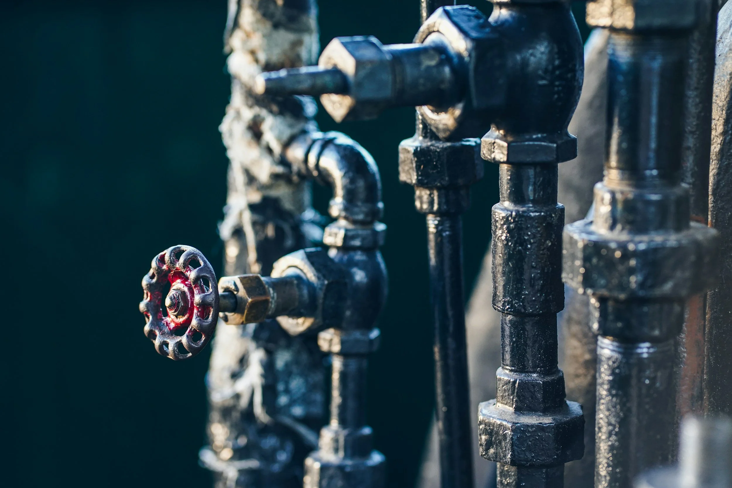 Close-up of black metal water pipes and valve handle with sunlight reflecting on surface.